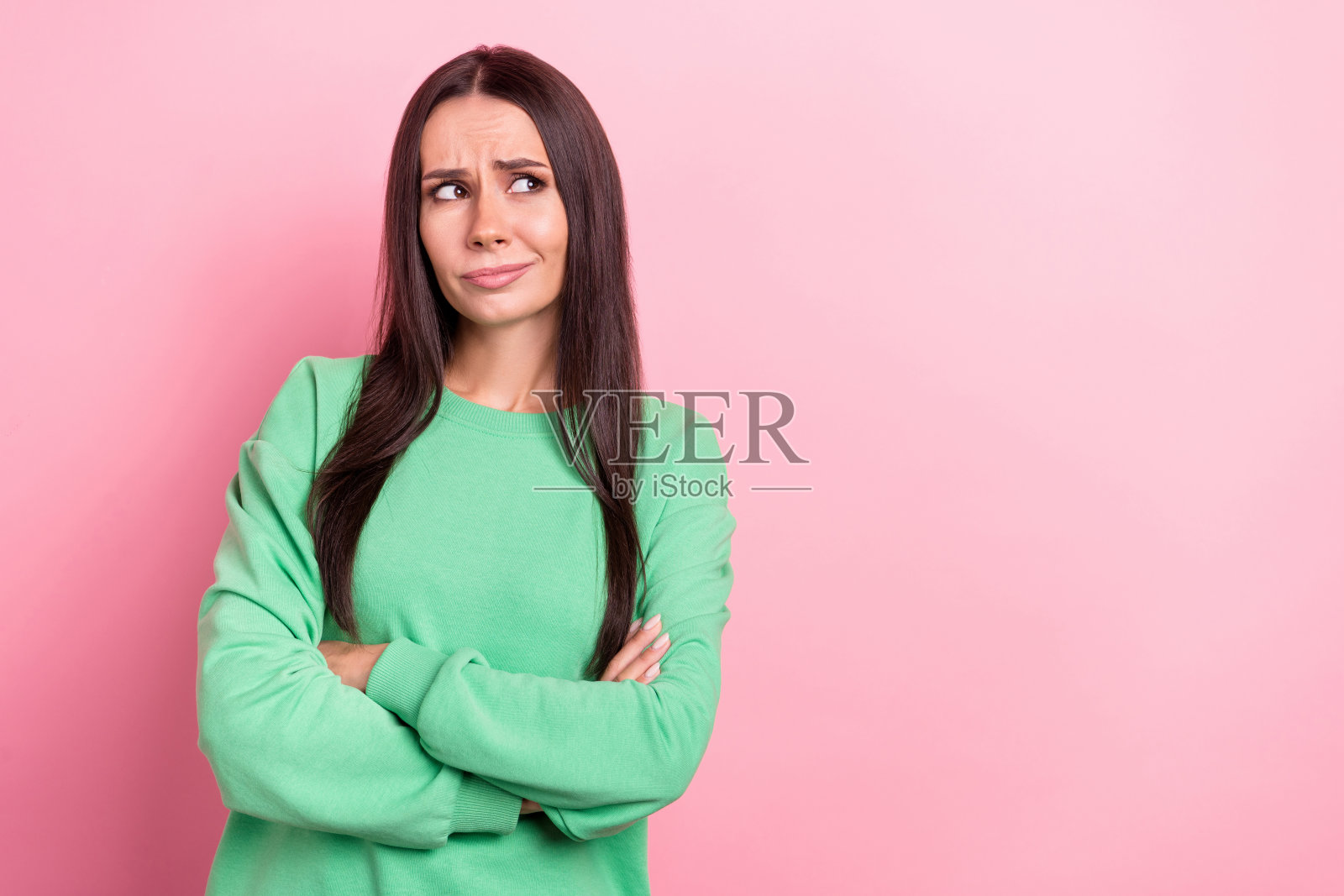 年轻的头脑聪明的沉思周到的女人穿着绿色套头衫的照片，双手交叉在粉红色的背景上看起来很孤立照片摄影图片