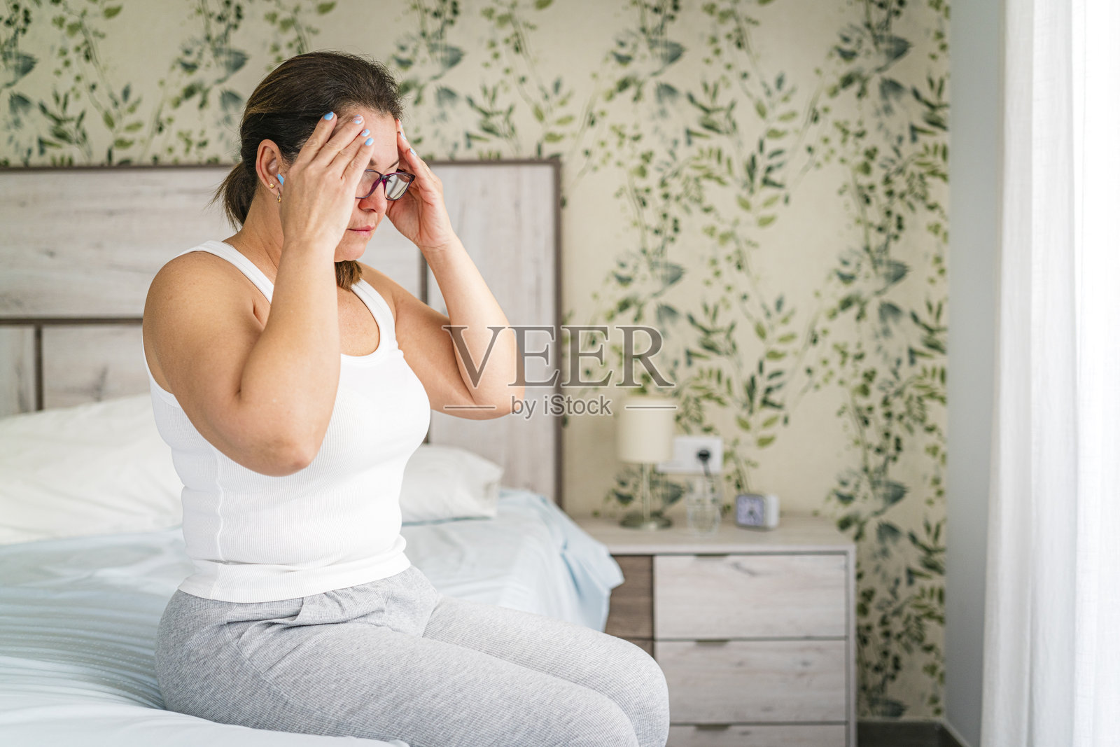 坐在床上的女人刚从头痛中醒来照片摄影图片