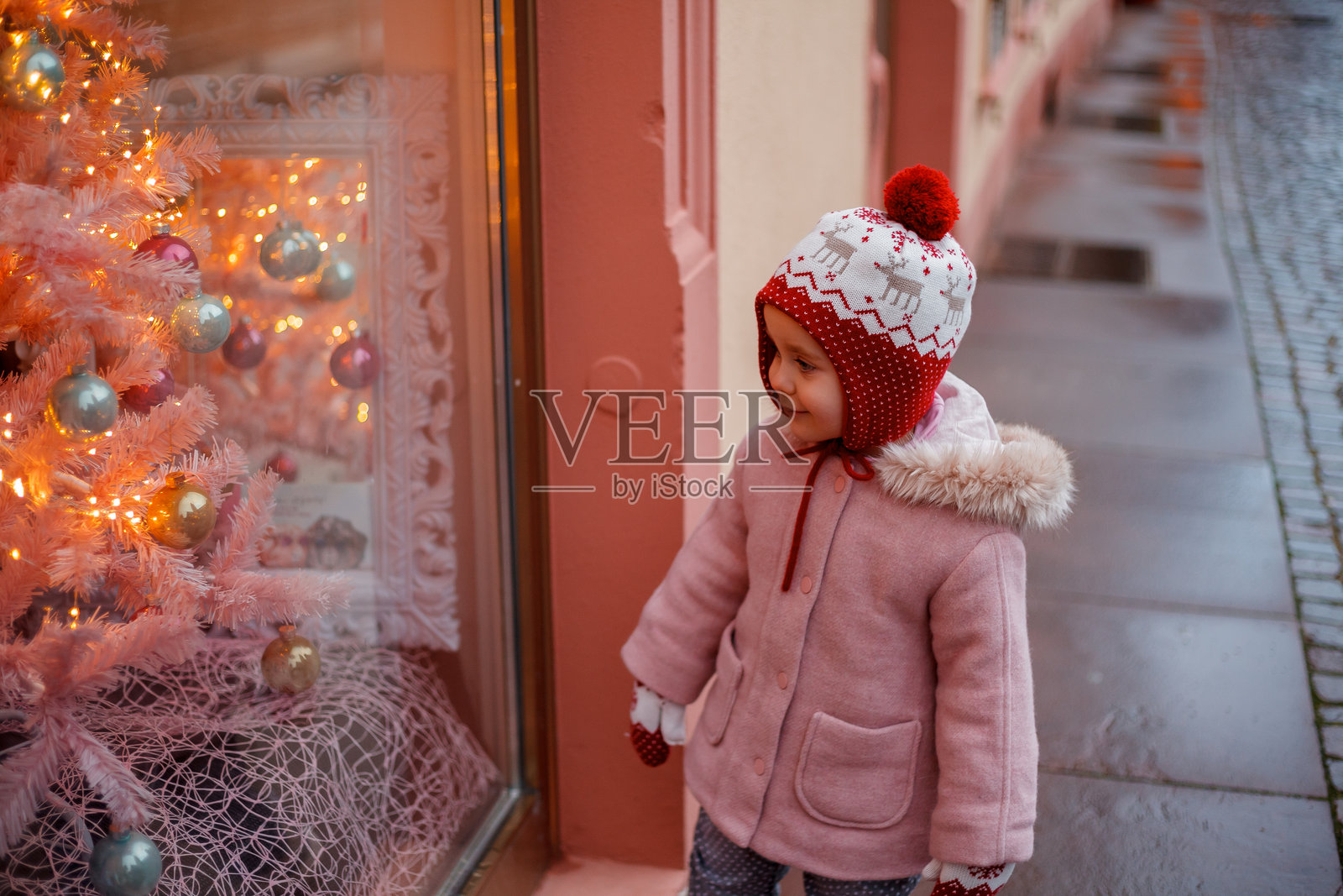 一个可爱的小女孩戴着帽子和手套站在欧洲城市的圣诞树旁。照片摄影图片