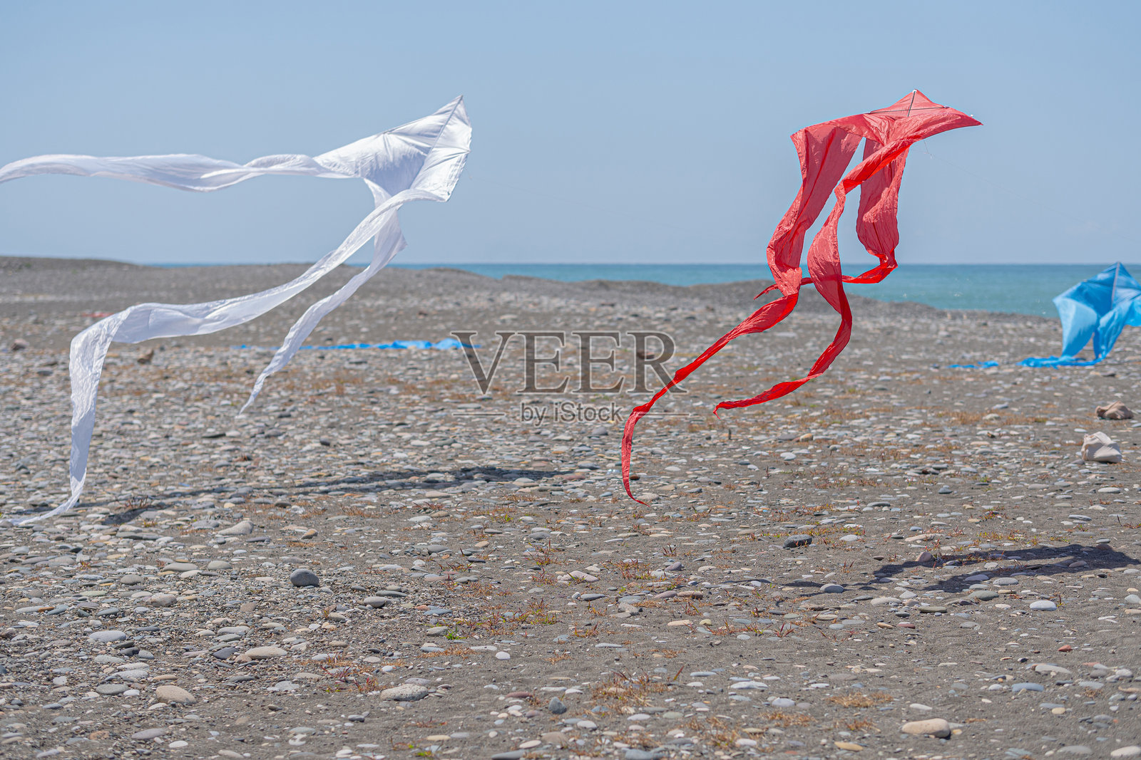 红色，白色和蓝色的风筝在卵石滩上。照片摄影图片