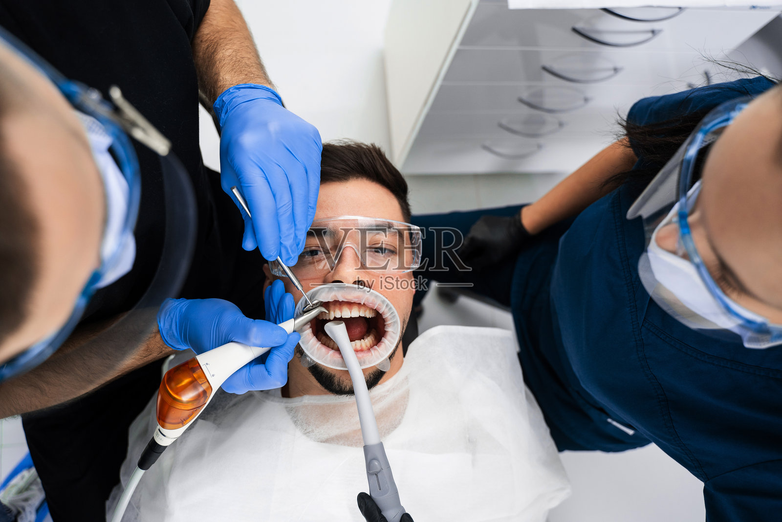 助理协助牙医在治疗前用气流仪准备牙齿。牙科诊所气流清洁牙齿。照片摄影图片