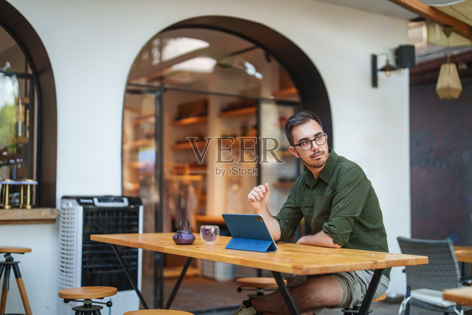 咖啡店生活的一天，一个男人在路边的咖啡馆里用着数码平板电脑，喝着凉茶。照片摄影图片