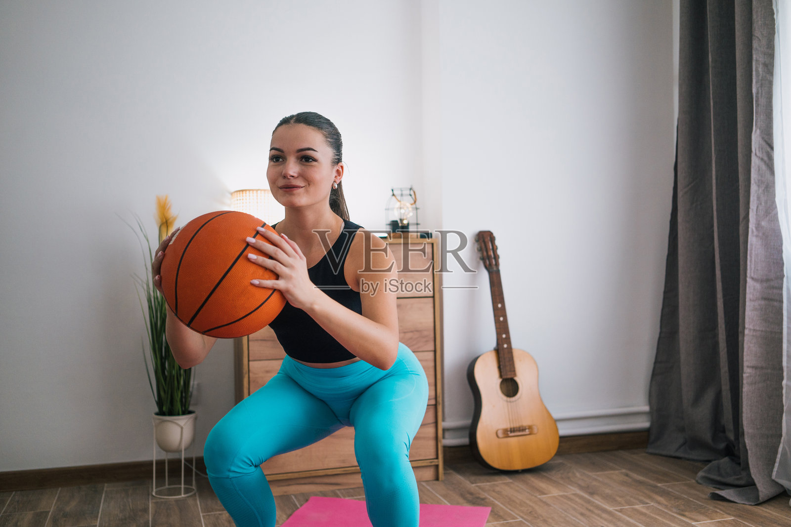 运动的年轻女子在做深蹲，手里拿着健身球照片摄影图片