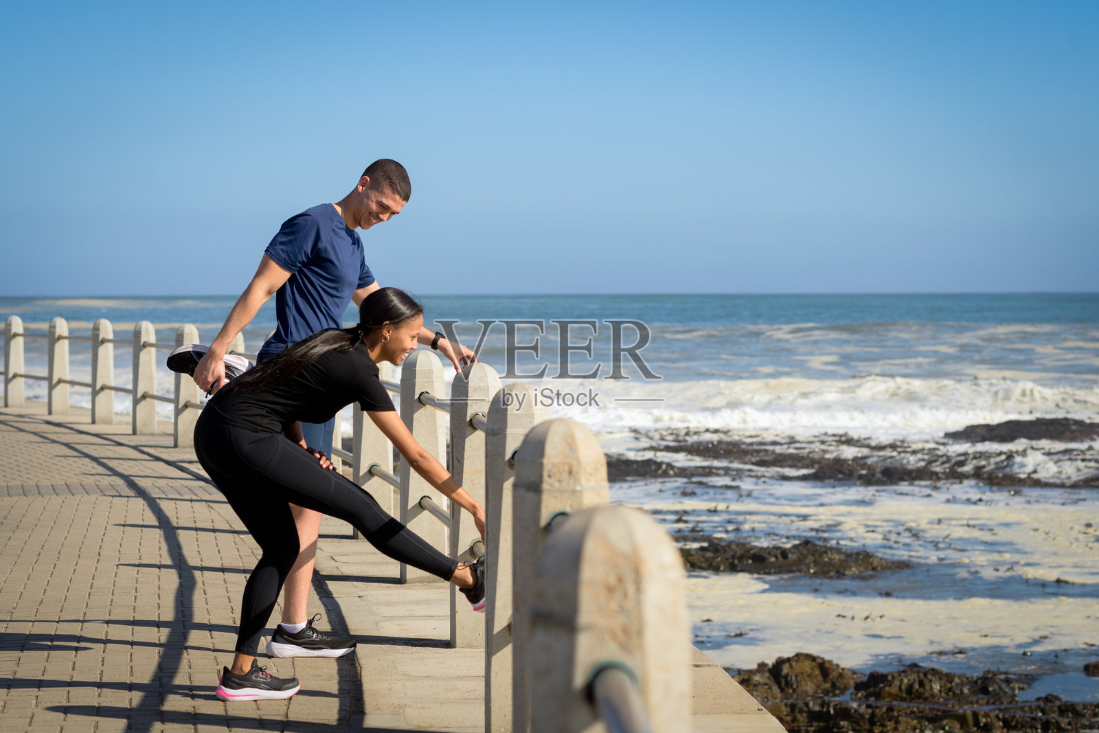阳光明媚的一天，一对异性恋情侣在海边散步时伸懒腰照片摄影图片
