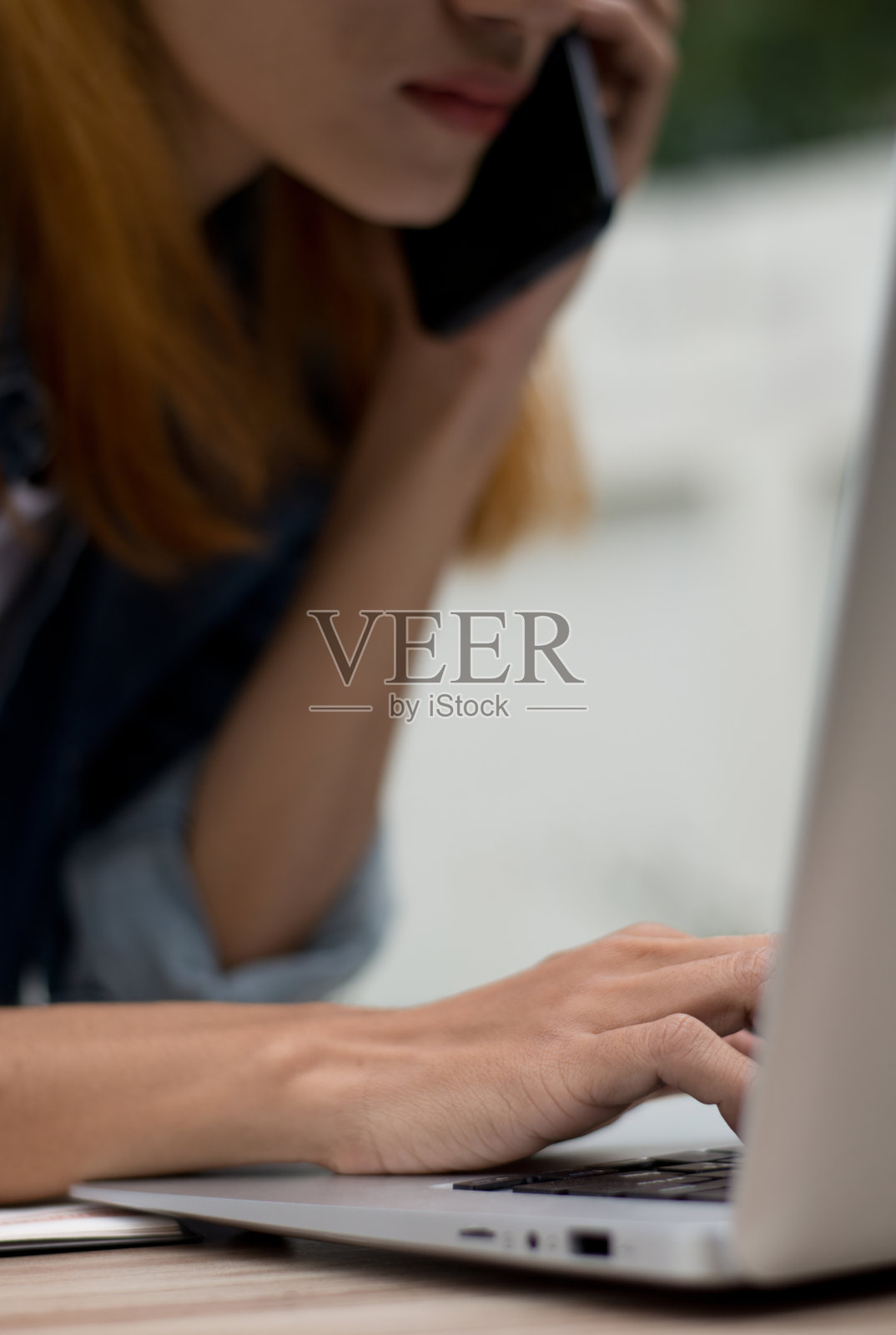 职业女性在手机和笔记本电脑上多任务处理。亚洲忙碌的女商人一边用电脑一边用智能手机通话的特写，展示了多任务处理和现代通信的垂直形象。照片摄影图片