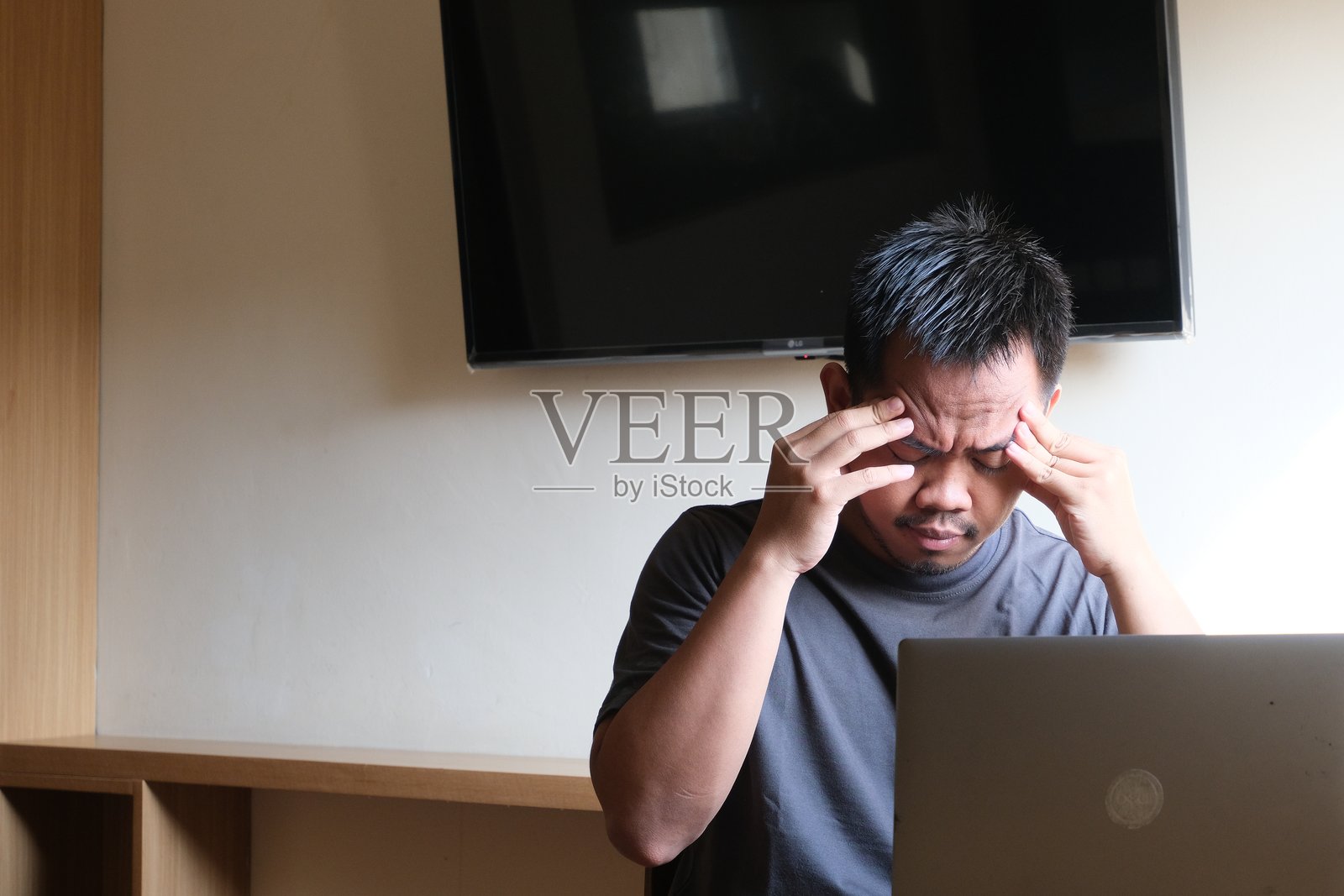 男性在头痛或压力大时，一边盯着笔记本电脑，一边用手指按压太阳穴，这凸显了精神疲劳和过度工作带来的挑战。照片摄影图片