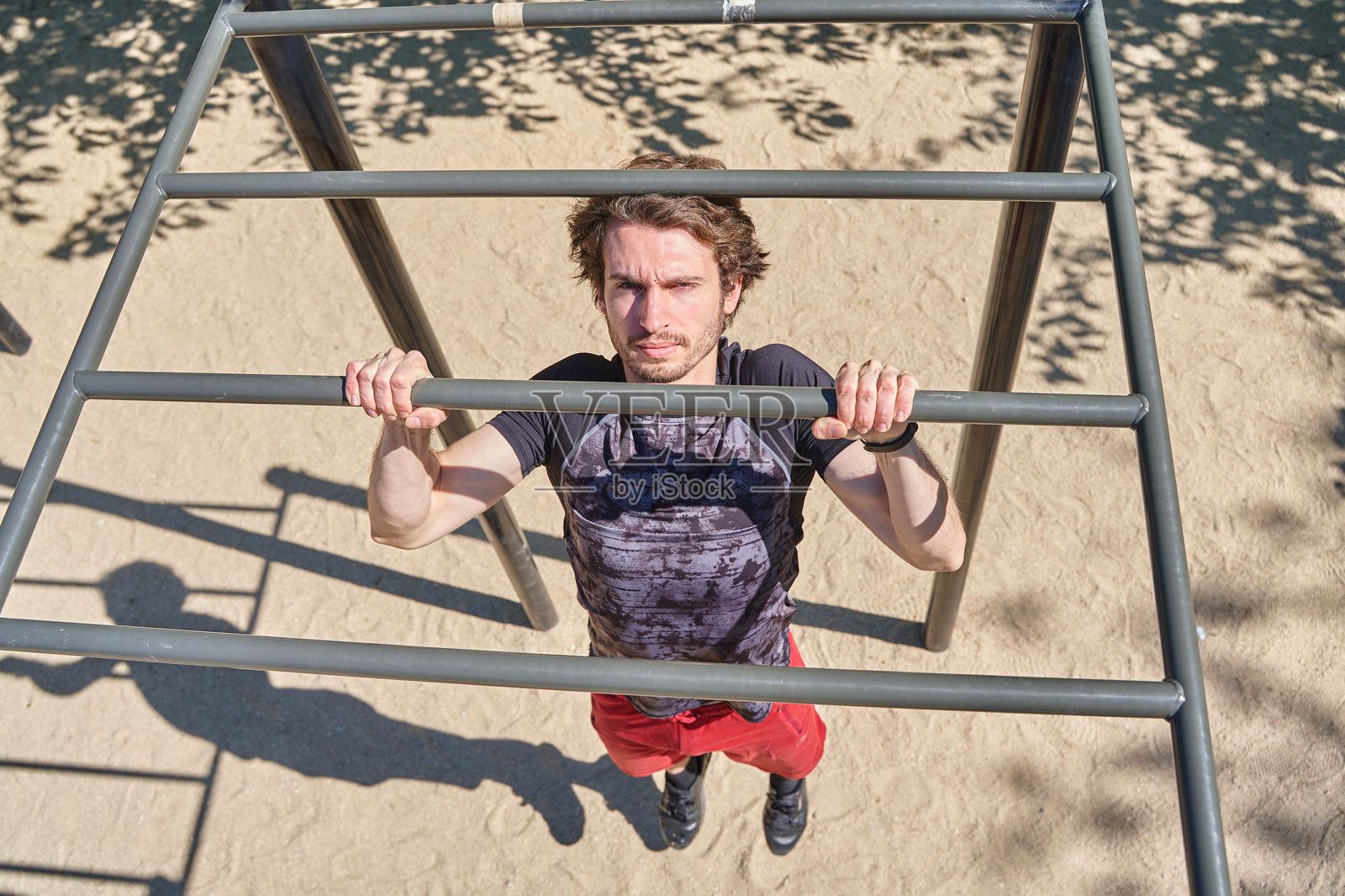 俯视图一名男跑步运动员在户外训练时在单杠上做引体向上，强壮的运动员穿着运动服在街头健身器材上锻炼，年轻的运动员在运动照片摄影图片