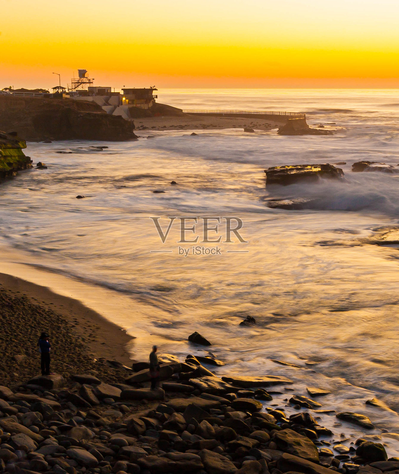 人们在岩石海滩上观看日落照片摄影图片