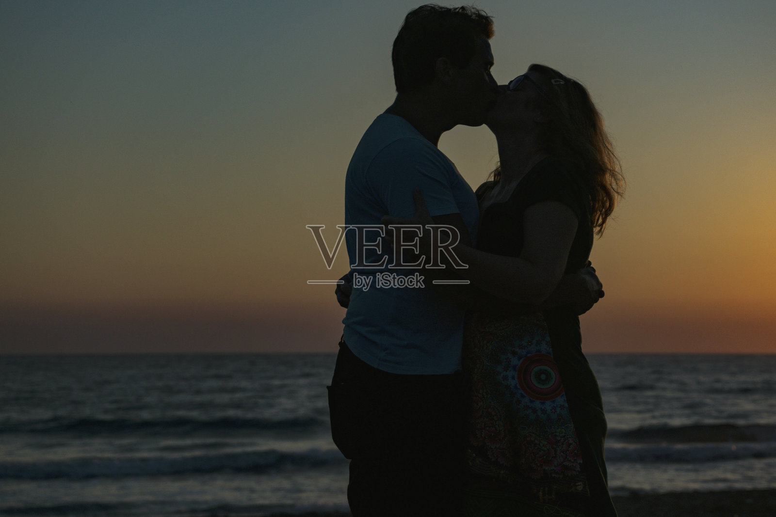 剪影夫妇在日落时站在海滩上照片摄影图片