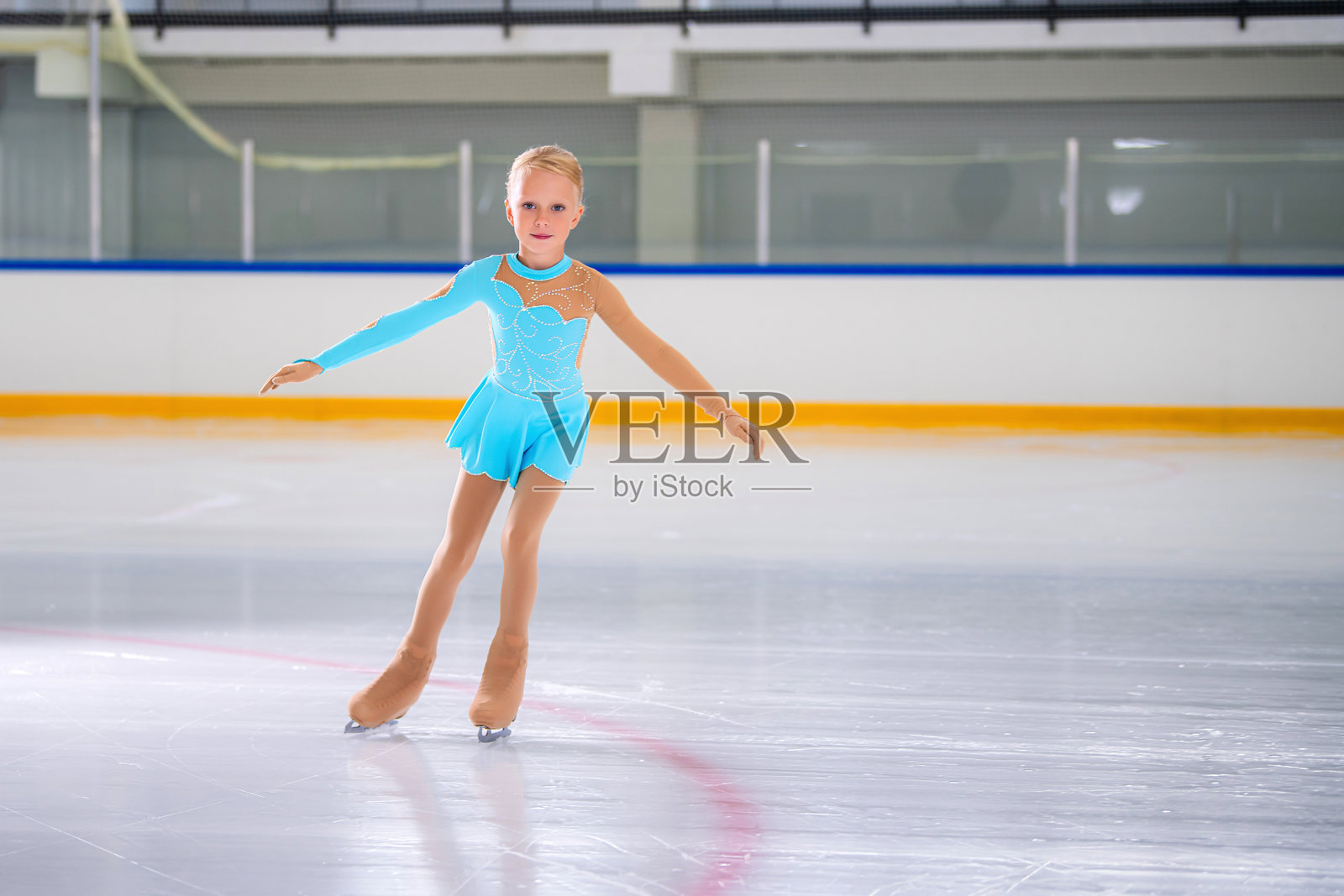 在表演期间，小女孩在室内溜冰场上做花样滑冰的全长肖像照片摄影图片