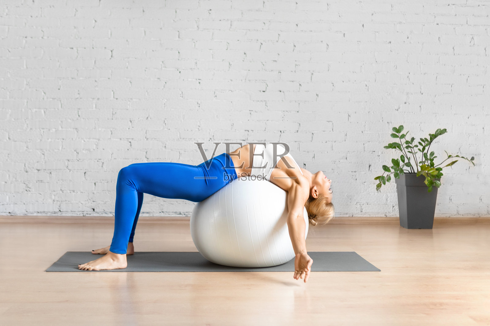 躺在健身球上放松背部的白人女性在室内阁楼工作室。照片摄影图片