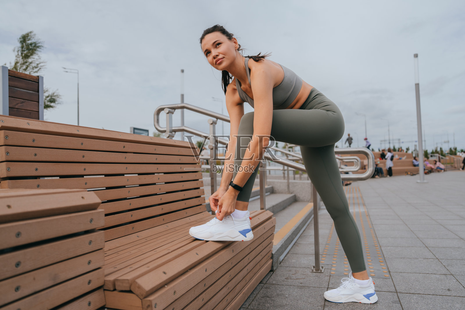 一位意志坚定的年轻女子在锻炼前系鞋带。穿着时髦的运动服，她准备在城市公园里健身照片摄影图片