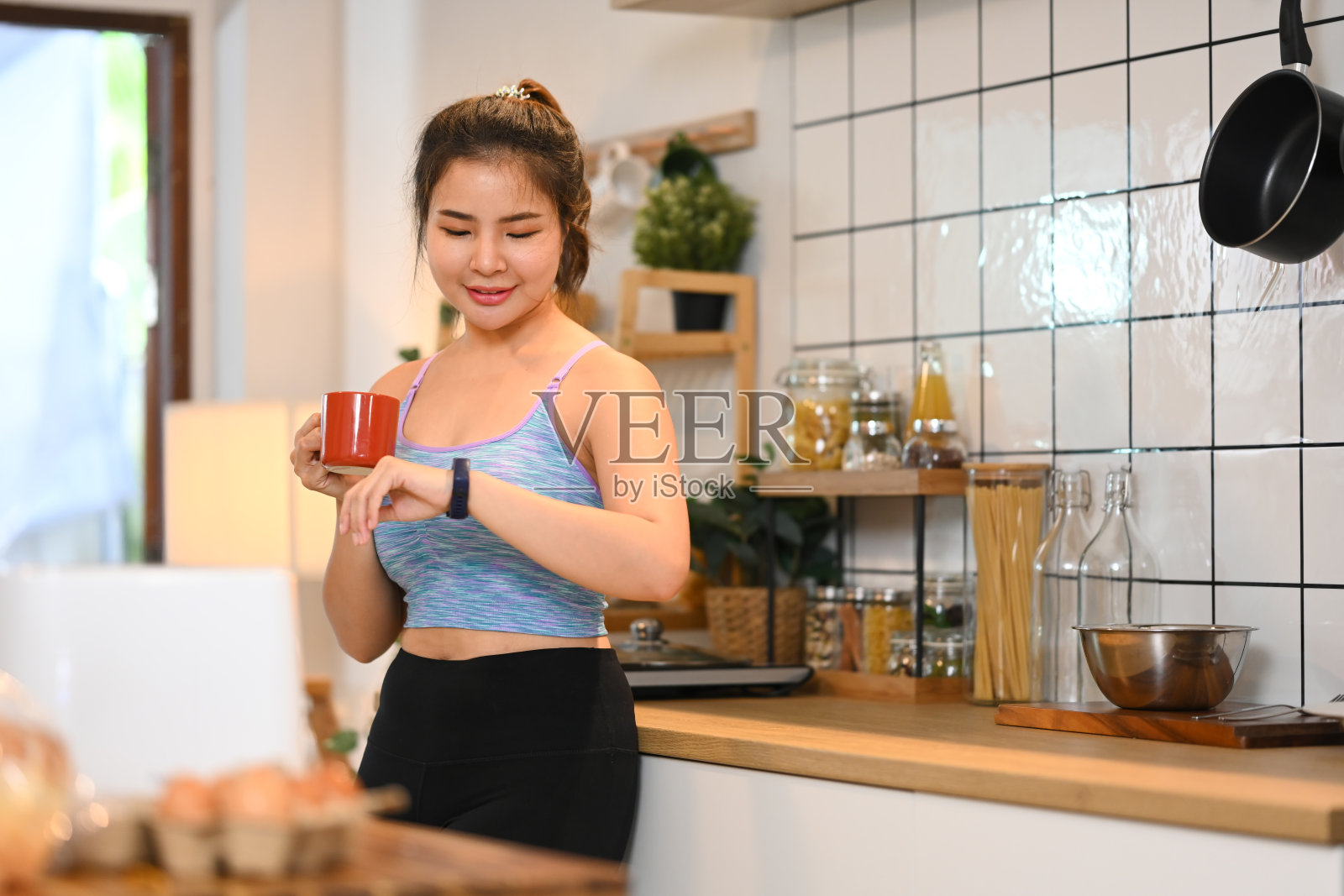 快乐的运动年轻女子喝着热茶，看手表的时间照片摄影图片