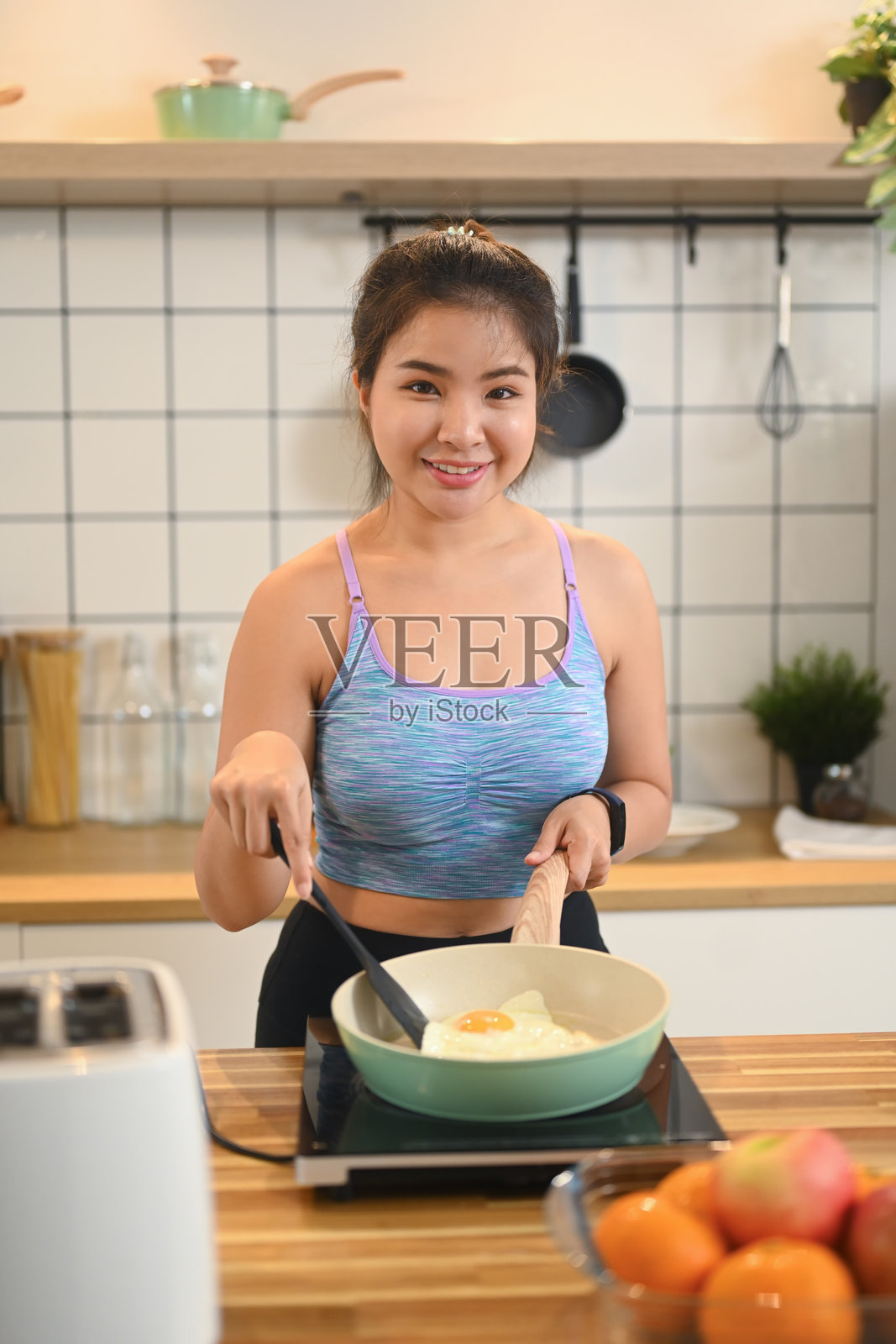 穿着运动服的亚洲年轻女子在家庭厨房煎鸡蛋当早餐的画像照片摄影图片