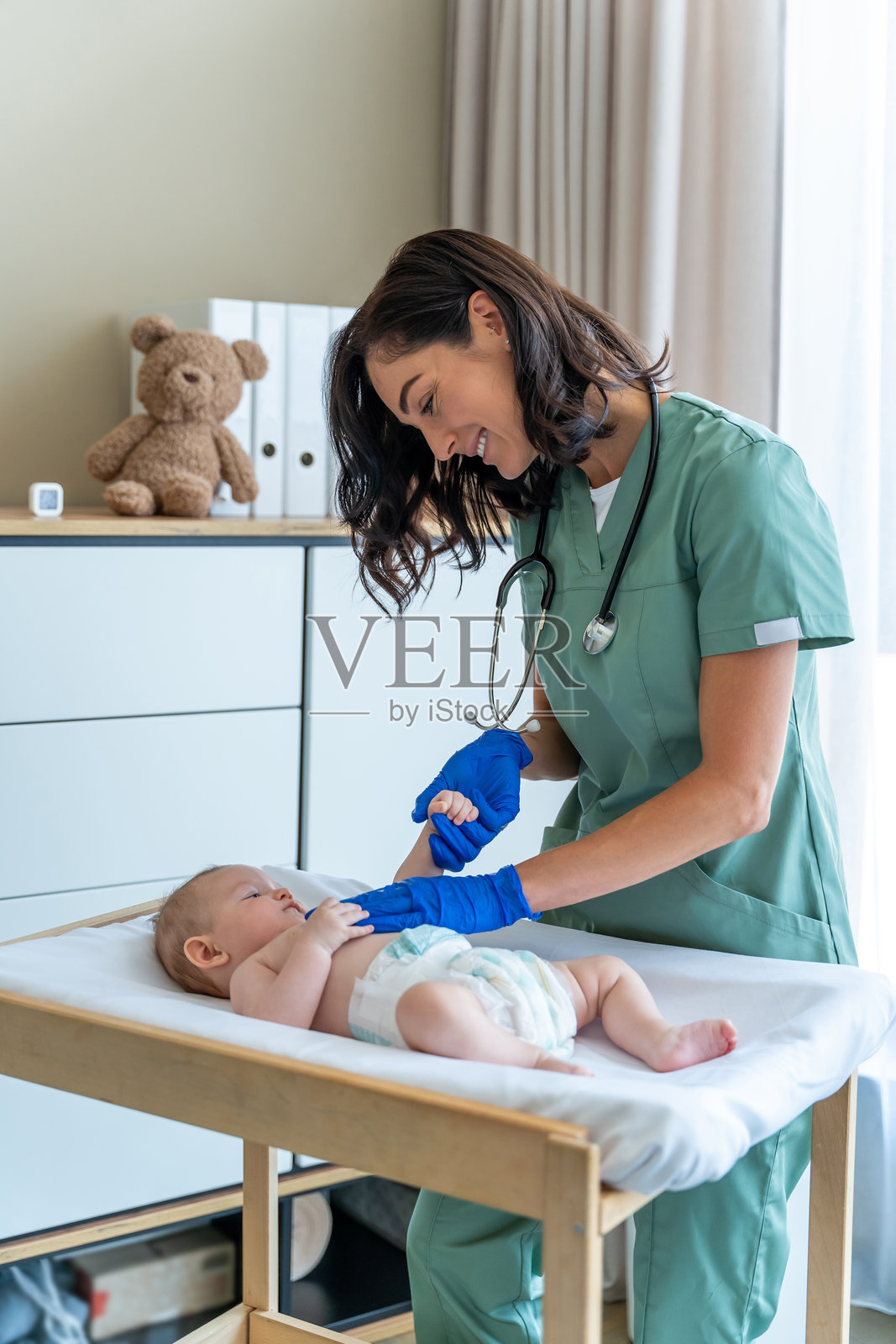 戴着蓝色手套微笑着的儿科医生在诊所里检查着抱着小手指的婴儿照片摄影图片