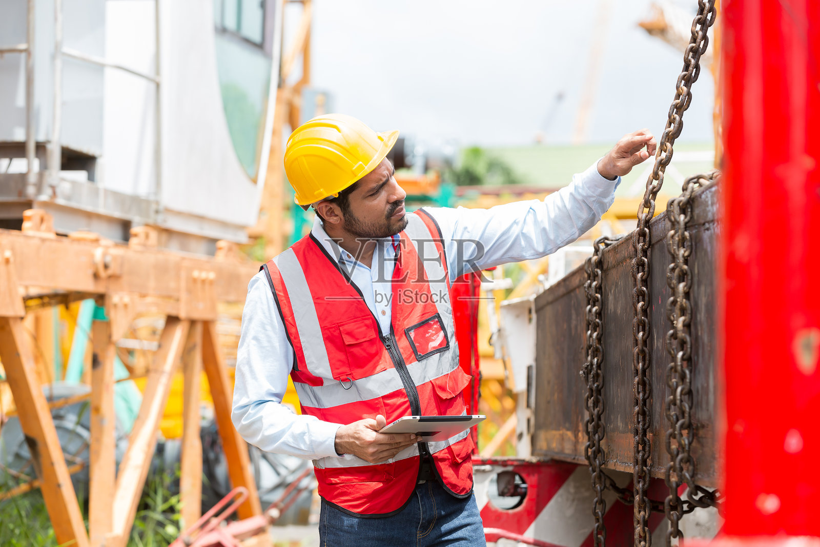 在建筑工地工作的亚洲男性建筑工人。从事数码平板电脑工作的男性工程师。男工程师在施工现场穿着安全制服和安全帽照片摄影图片