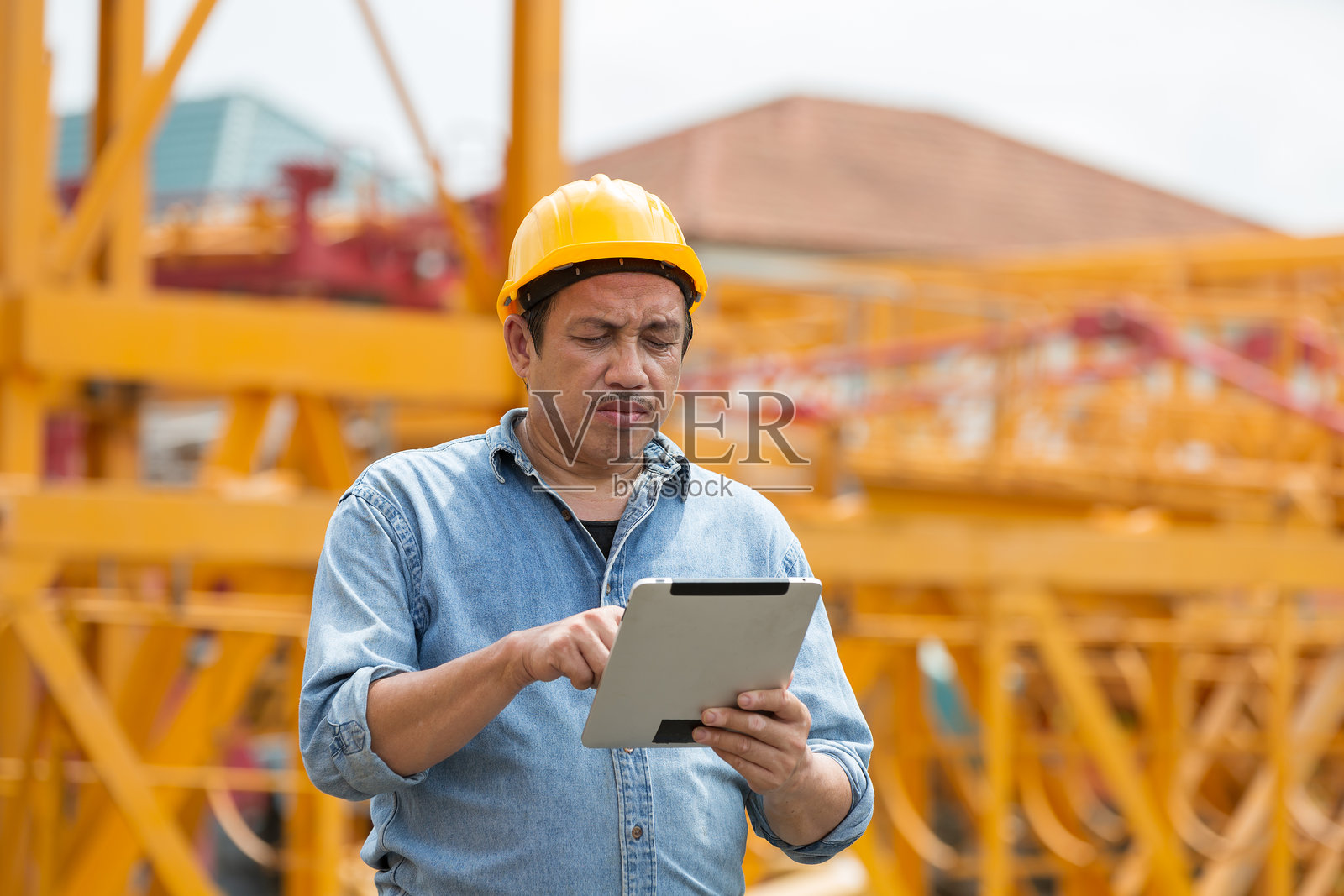 在建筑工地工作的亚洲男性建筑工人。从事数码平板电脑工作的男性工程师。男工程师在施工现场穿着安全制服和安全帽照片摄影图片