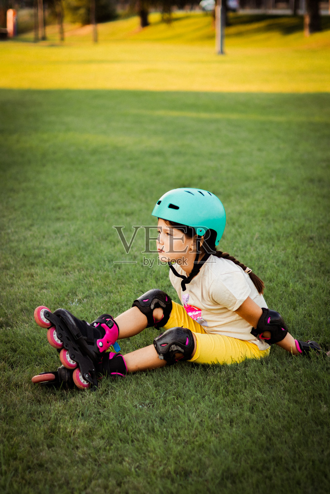 在公司大楼附近的公园里，戴着防护装备和头盔，穿着直排轮滑鞋的漂亮好动的女学生照片摄影图片