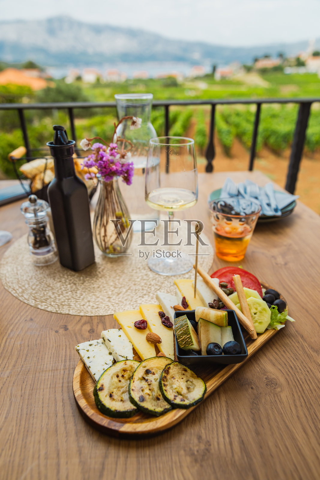 特写一盘什锦奶酪和水果和妇女享受葡萄酒和奶酪在风景优美的葡萄园露台照片摄影图片