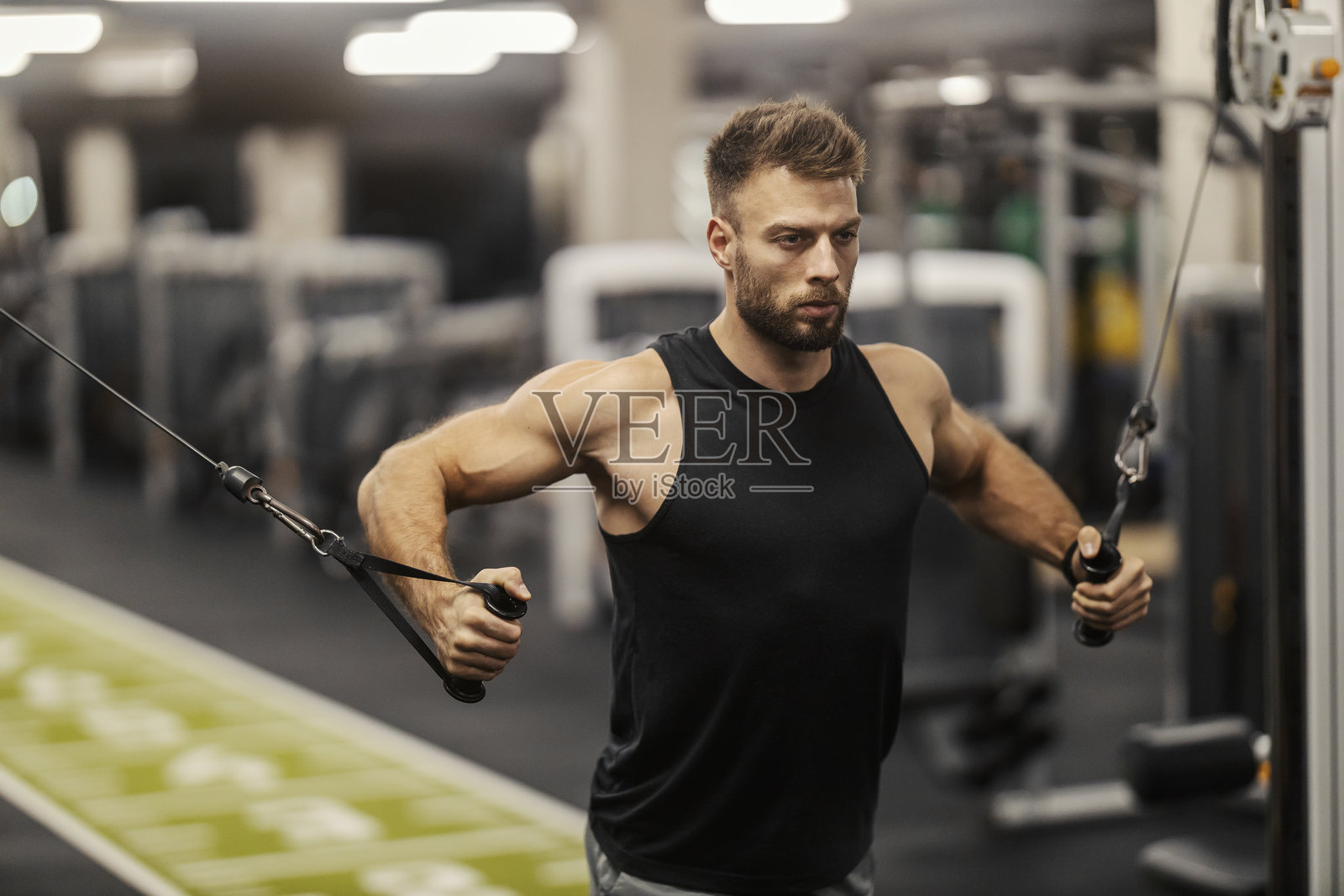 强壮的男性运动员在健身房的健身器上练习他的肩膀和二头肌。照片摄影图片