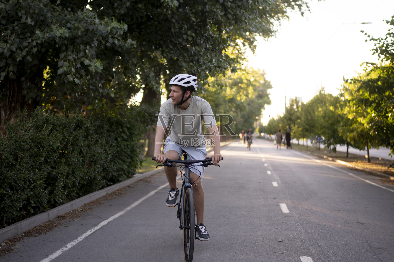 白天，戴着头盔的运动员骑着公路自行车在公园里的一条铺好的小路上骑行照片摄影图片