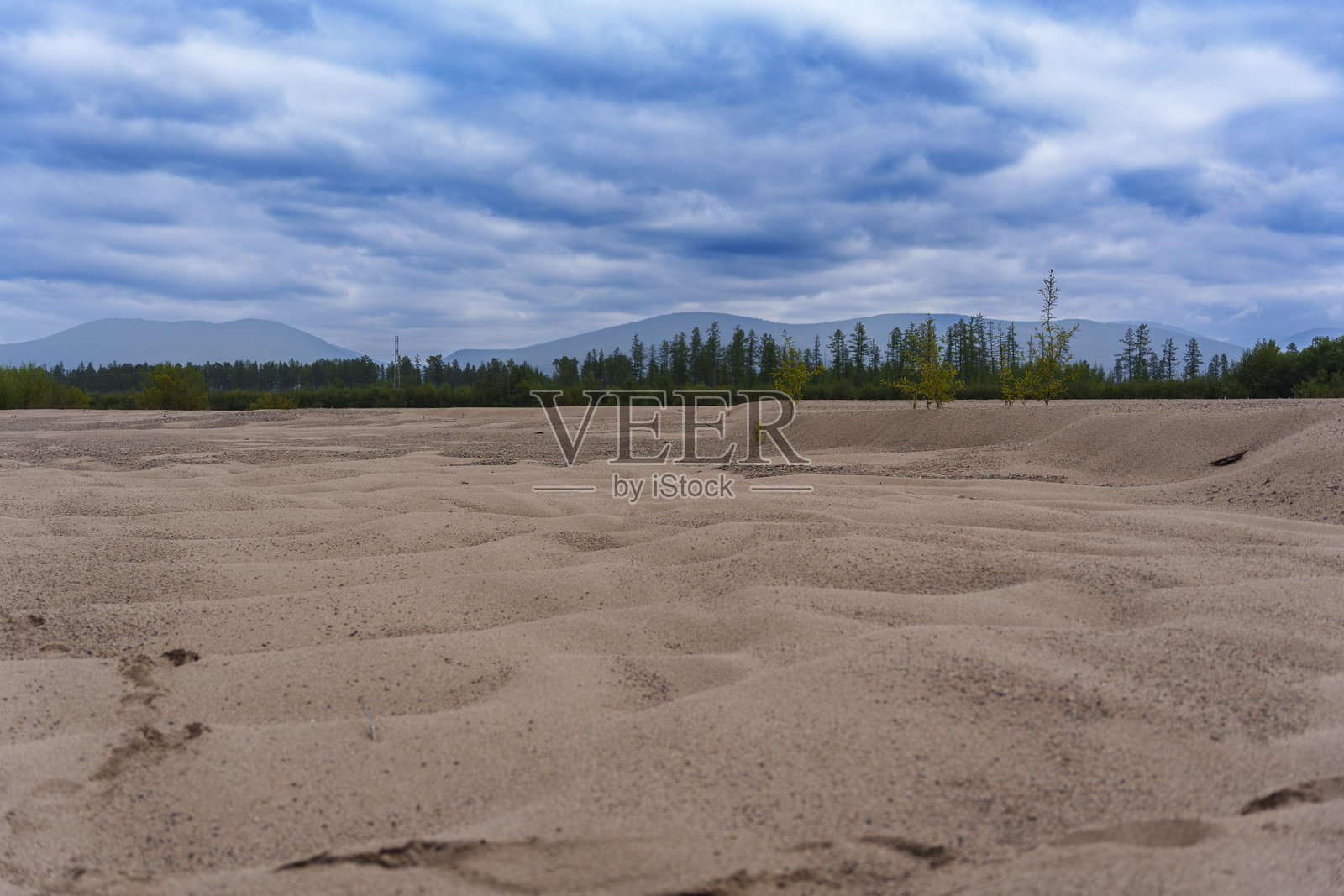多云的天空下，有森林和山脉的沙质地形照片摄影图片