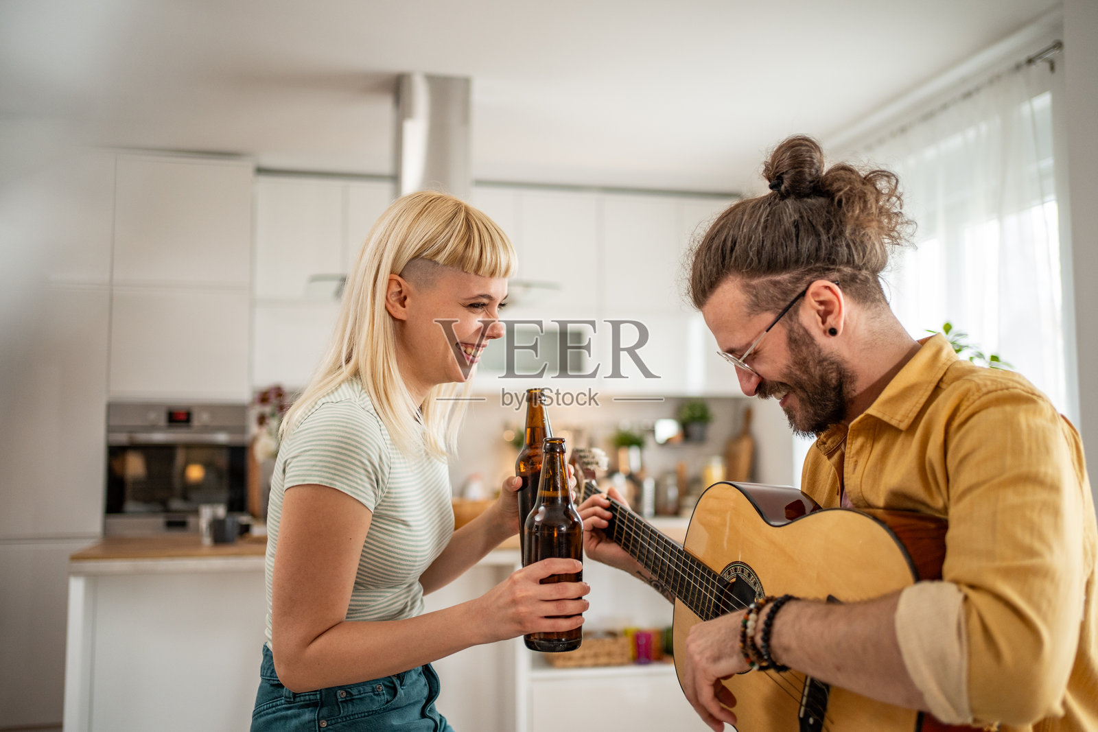 这对夫妇在他们的客厅里度过了快乐的一天，喝着啤酒，弹着吉他照片摄影图片