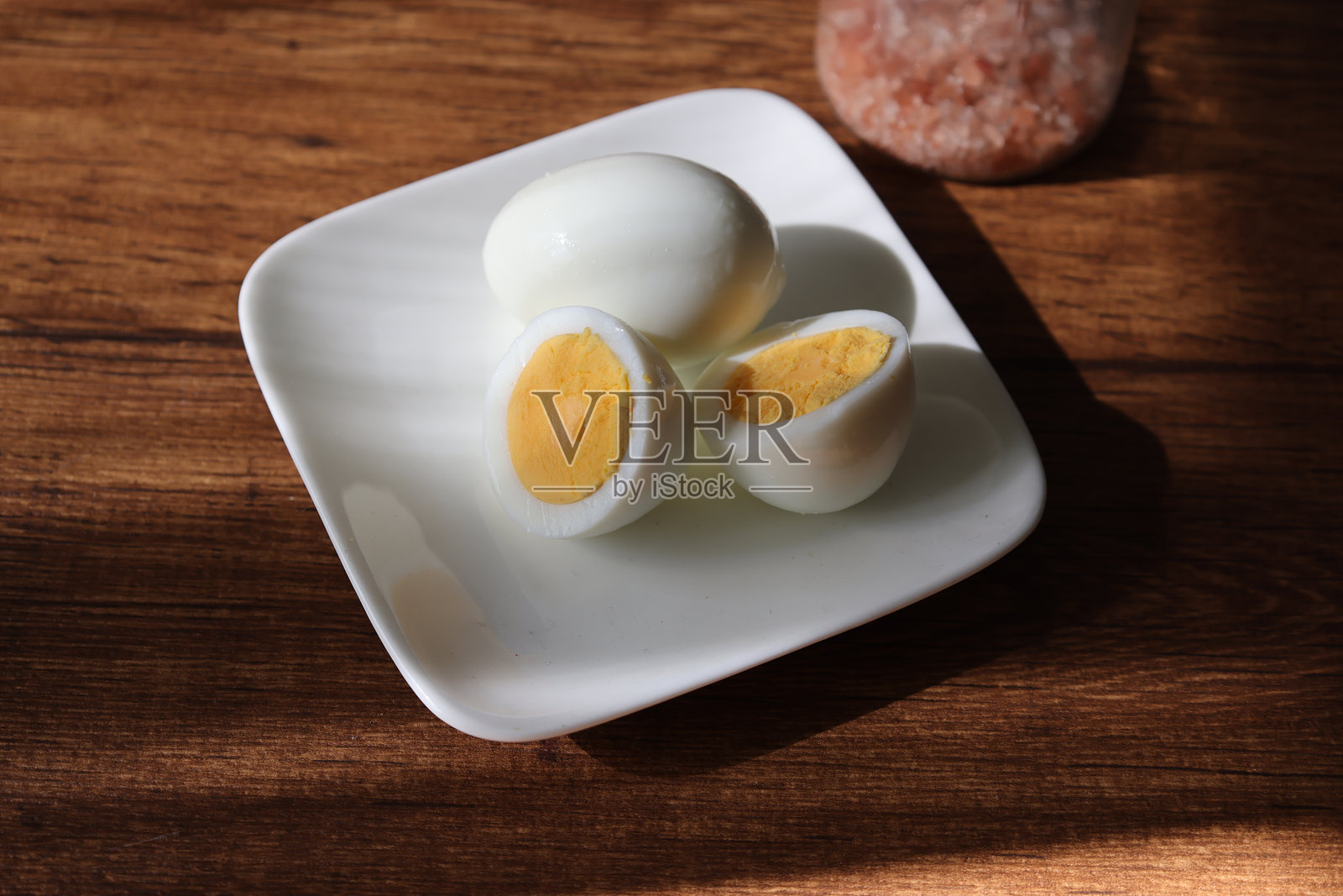 木桌上放着盐，盘子里放着煮熟的鸡蛋。照片摄影图片