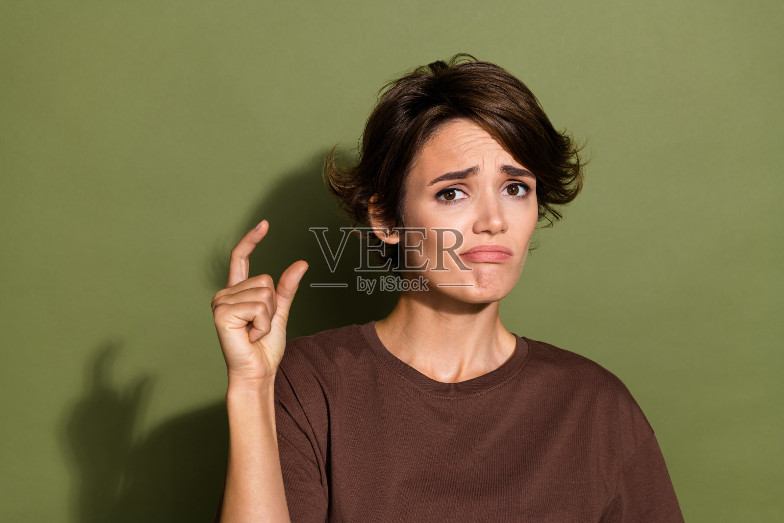 失望的女人，短发，穿着棕色t恤，对她的期望不满意，在卡其色背景上孤立照片摄影图片