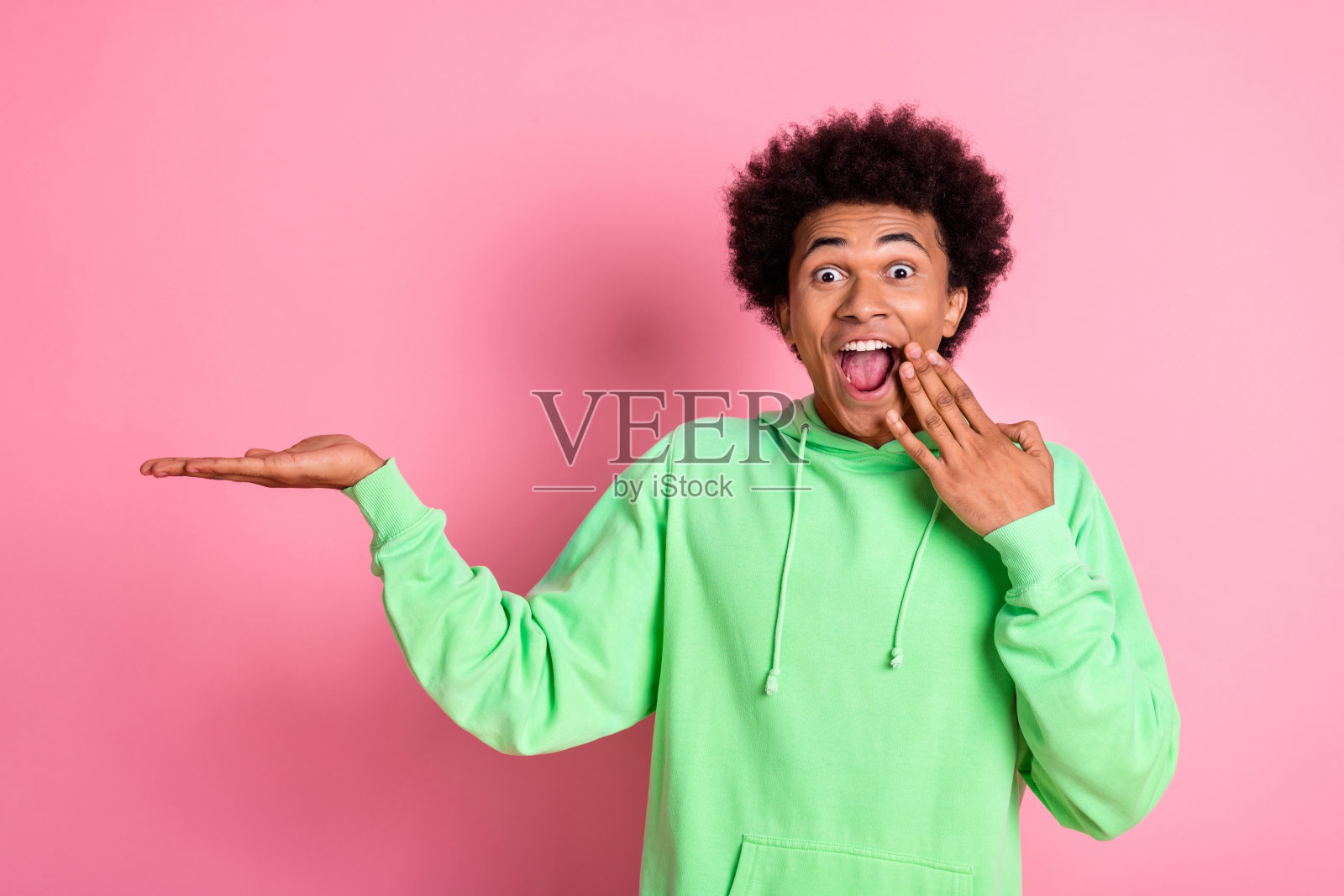 酷酷的年轻人的肖像持有空白空间穿绿色卫衣孤立在粉红色的背景照片摄影图片