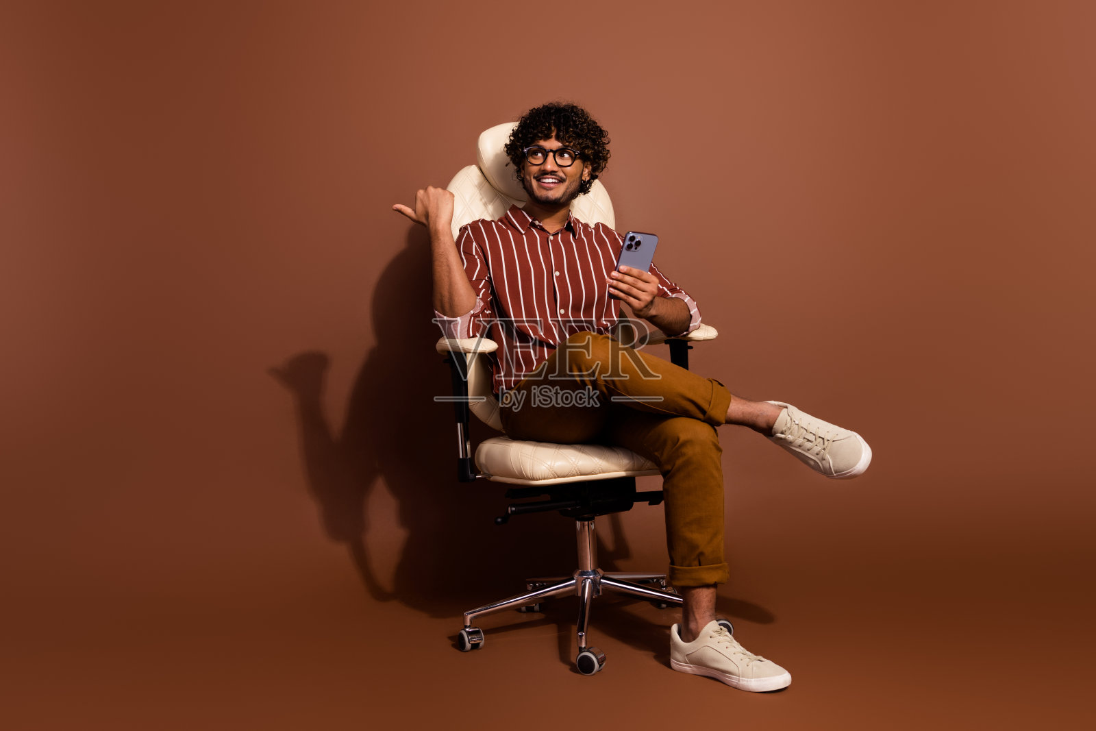 漂亮的年轻人的全尺寸照片坐在椅子上直接手指空的空间穿衬衫孤立的棕色背景照片摄影图片