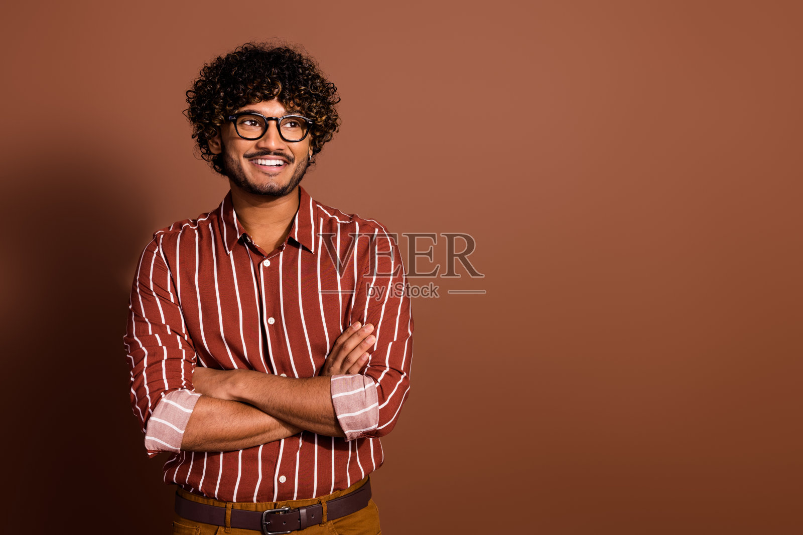 照片上漂亮的年轻人双手交叉，看起来空无一人，穿着条纹衬衫孤立在棕色背景上照片摄影图片