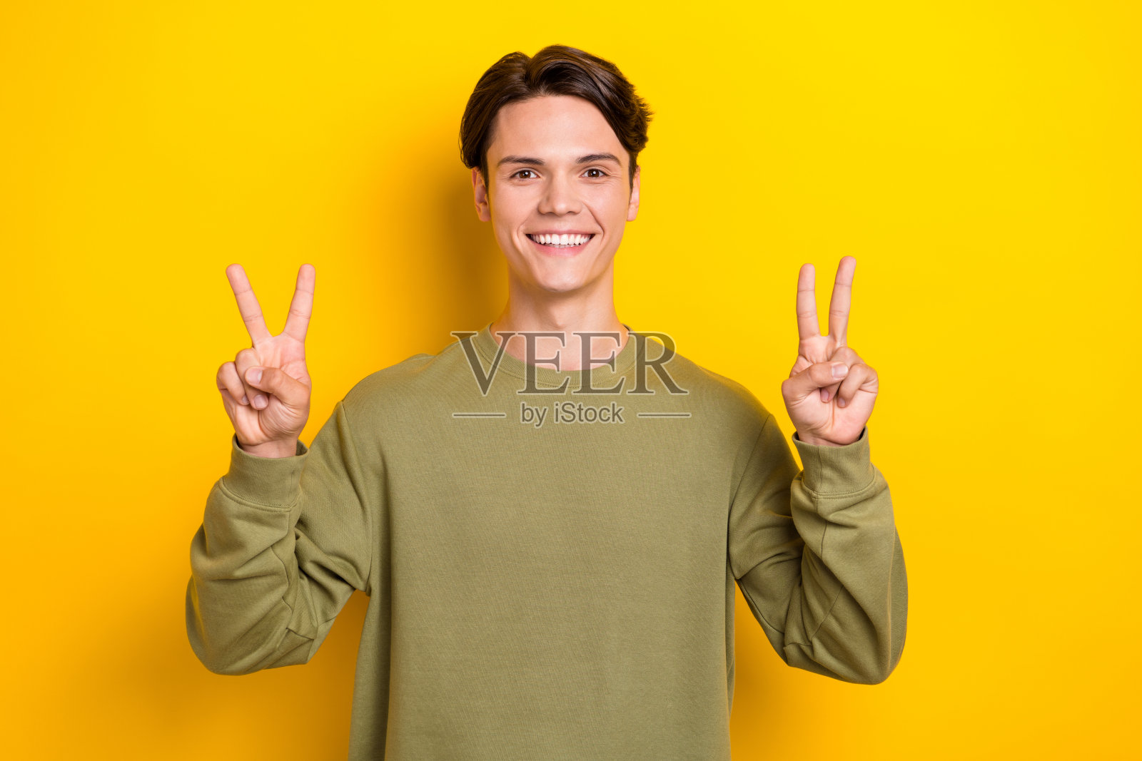 照片中，一个满意的人微笑着，双手手指在黄色背景上表现出v型手势照片摄影图片