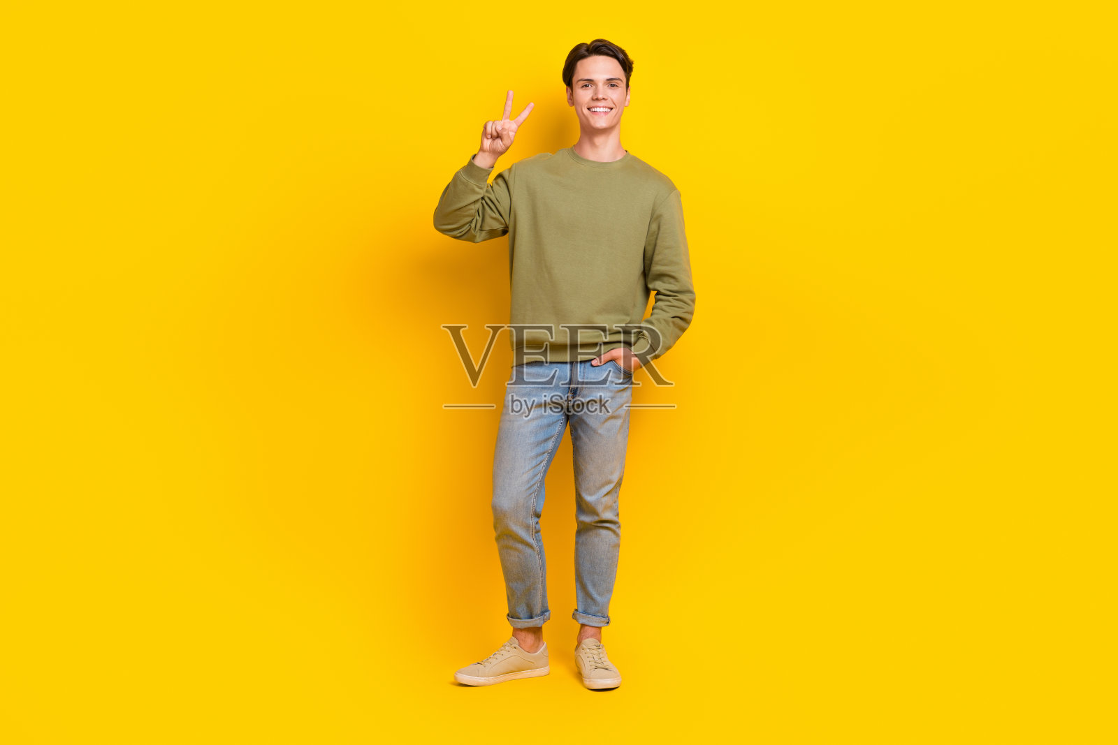 欢快的年轻男子的全身肖像，手的手指显示v字形孤立在黄色背景照片摄影图片
