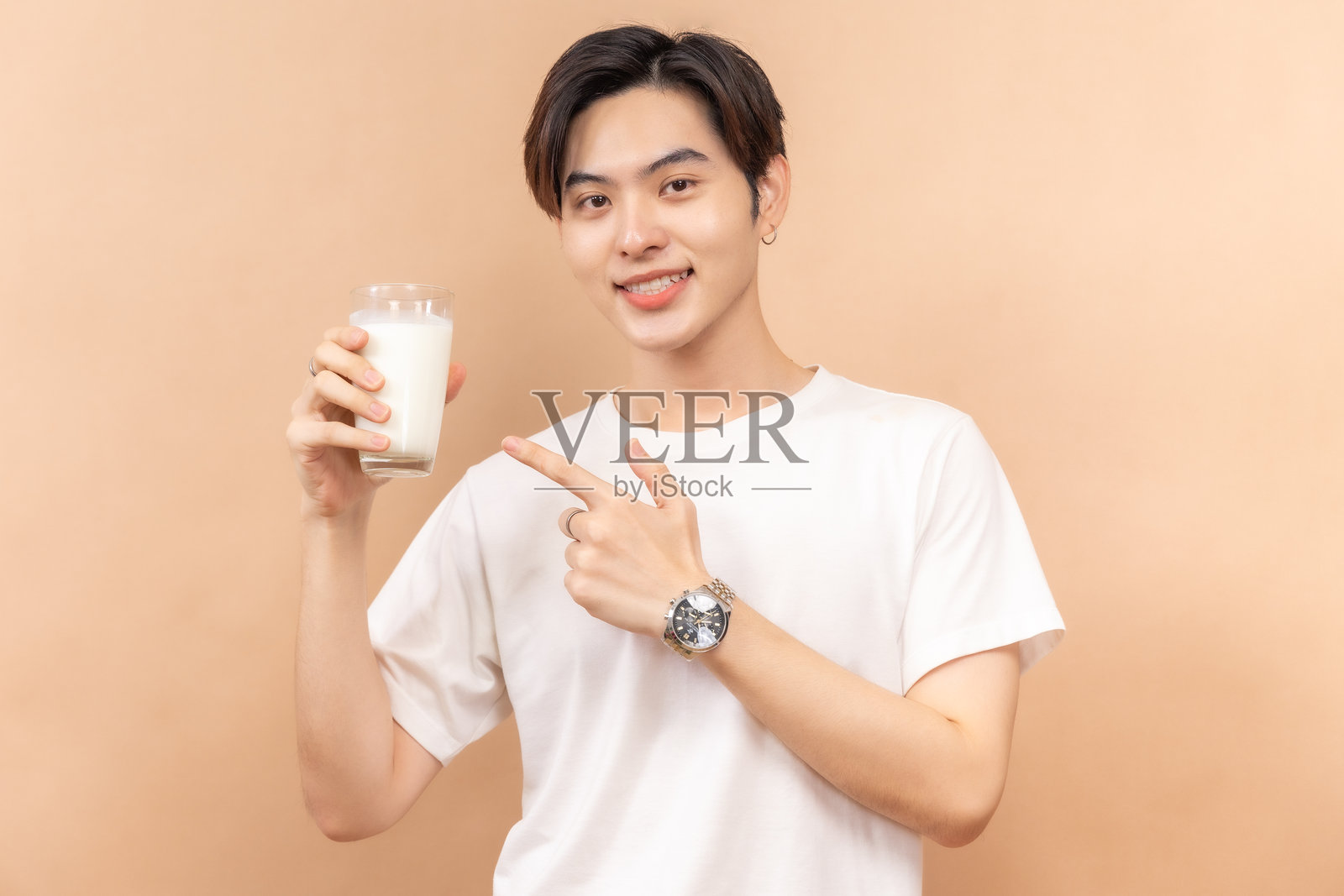 一个穿着白衬衫的快乐的亚洲人，拿着几杯牛奶和一碗沙拉，背景是米色。照片摄影图片