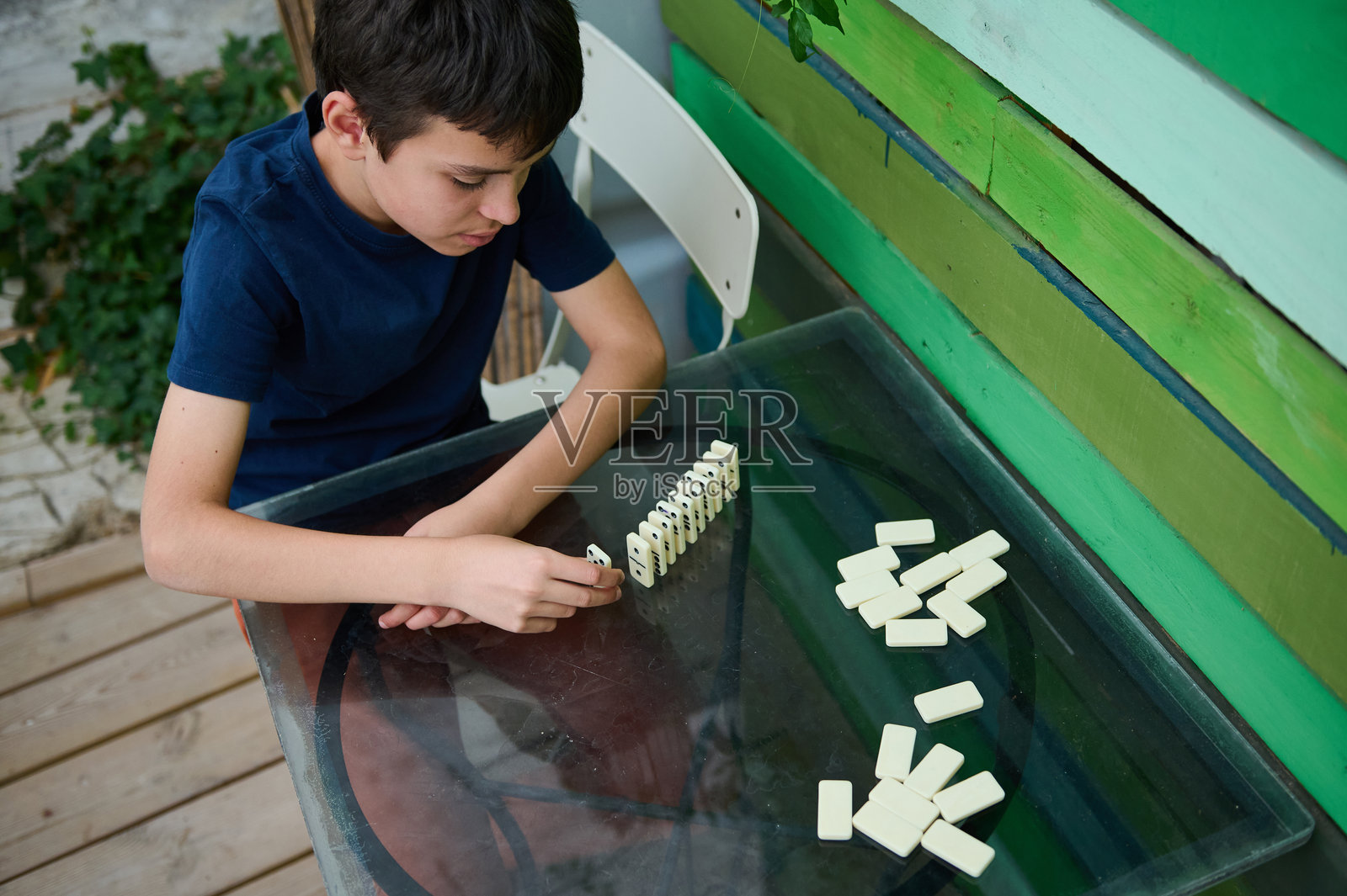 小男孩专注于在桌子上玩多米诺骨牌，从事户外活动，在平静、自然的环境中表现出专注和策略照片摄影图片