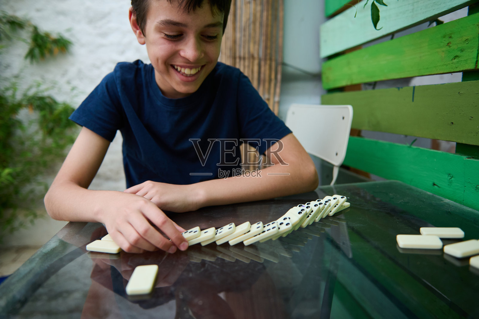 微笑的男孩在户外的桌子上玩多米诺骨牌，享受休闲时间的战略游戏，在轻松的环境中被丰富多彩的自然元素所包围。照片摄影图片