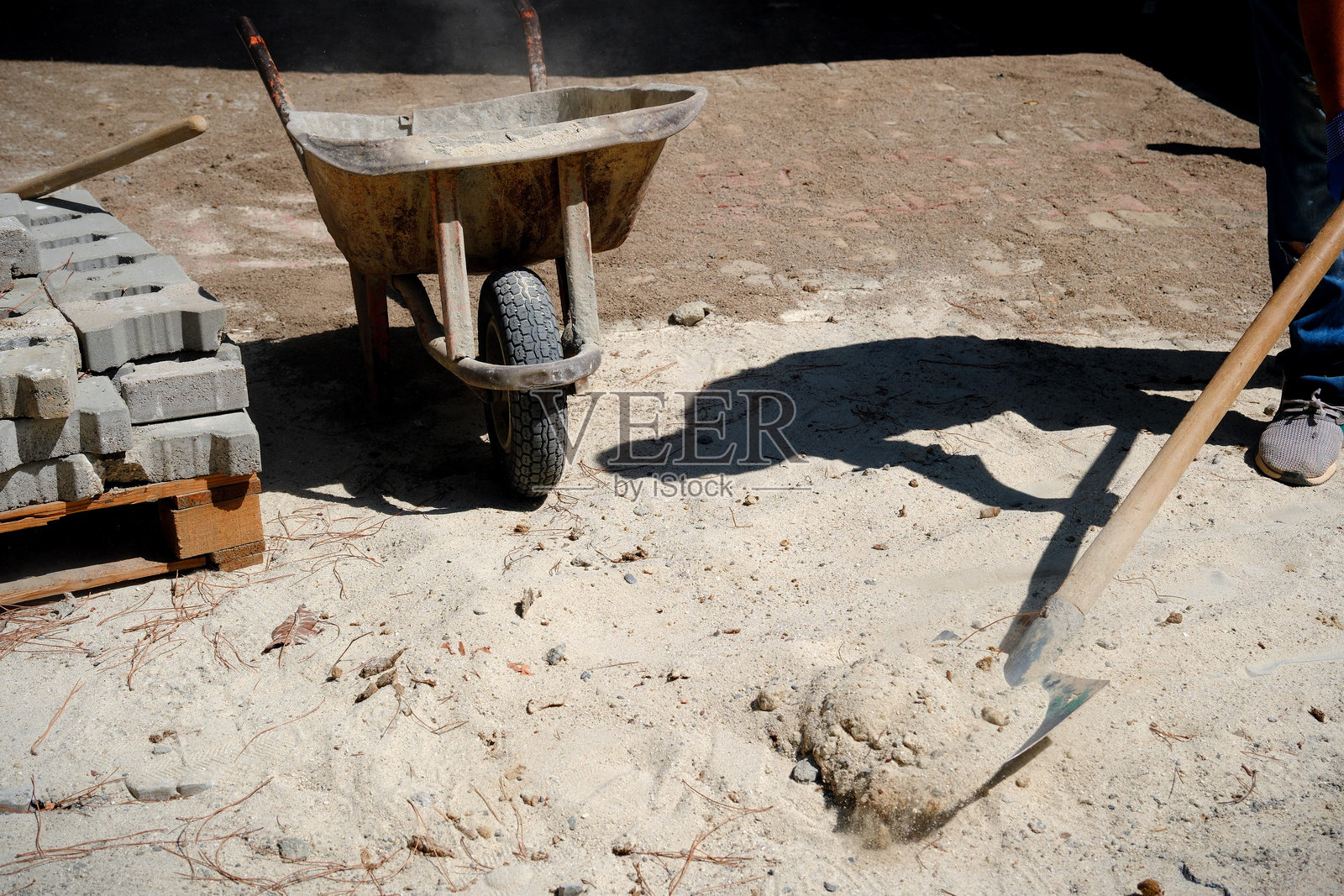 在铺路工作中，一名工人用铲子把泥土扔进手推车照片摄影图片