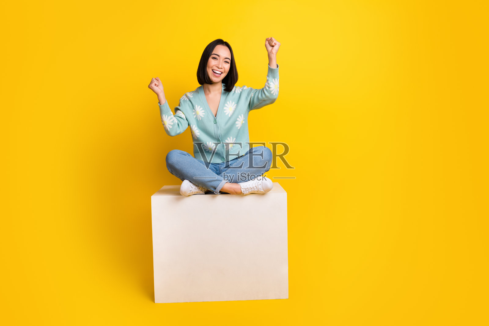 大喜大喜满意的女人的全尺寸照片蓝色套头衫坐在立方体上握紧拳头孤立的黄色背景照片摄影图片