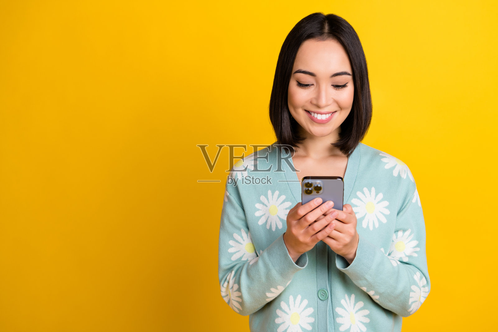 照片积极乐观可爱的女人与鲍勃发型穿着蓝色套头衫打字短信手机孤立的黄色背景照片摄影图片