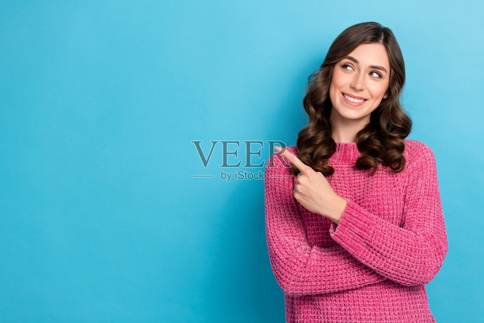 照片中华丽开朗的女士穿着粉红色时髦的衣服，手臂上展示了蓝色背景上的空旷凉爽照片摄影图片