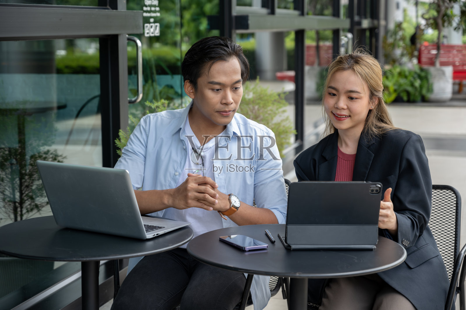 两个商人在一家现代咖啡店里用平板电脑和笔记本电脑讨论工作。照片摄影图片