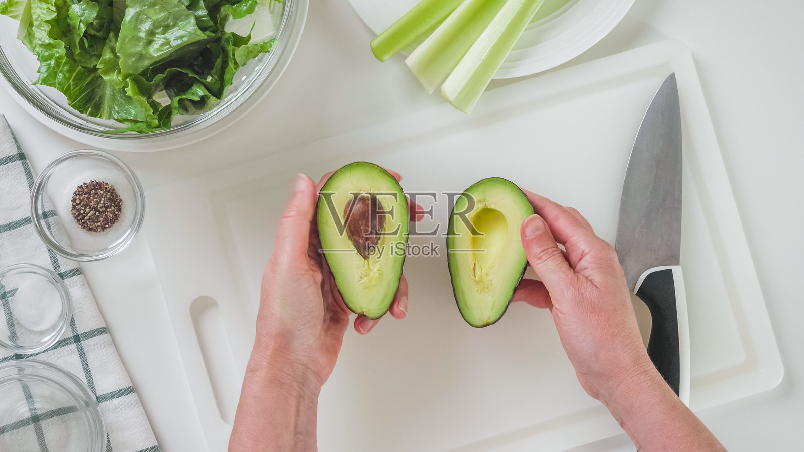 两个牛油果在女人的手里。绿色沙拉食谱，配料在白色背景上照片摄影图片