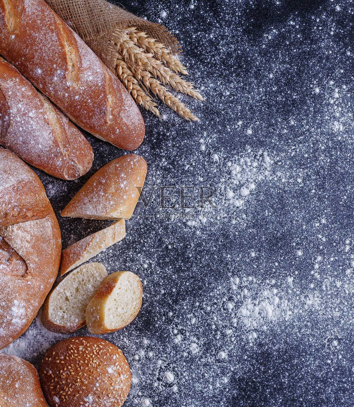 面包-黑色黑板背景上的金色乡村硬皮面包和小圆面包。照片摄影图片