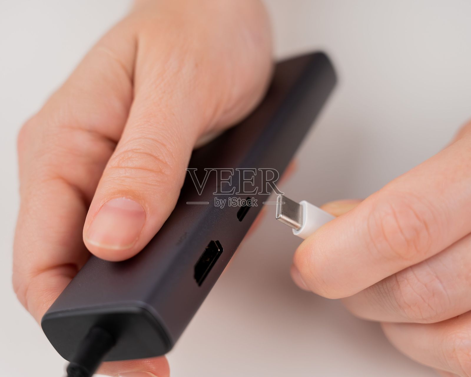 一名妇女将一根白色的C型电缆插入黑色的端口。照片摄影图片