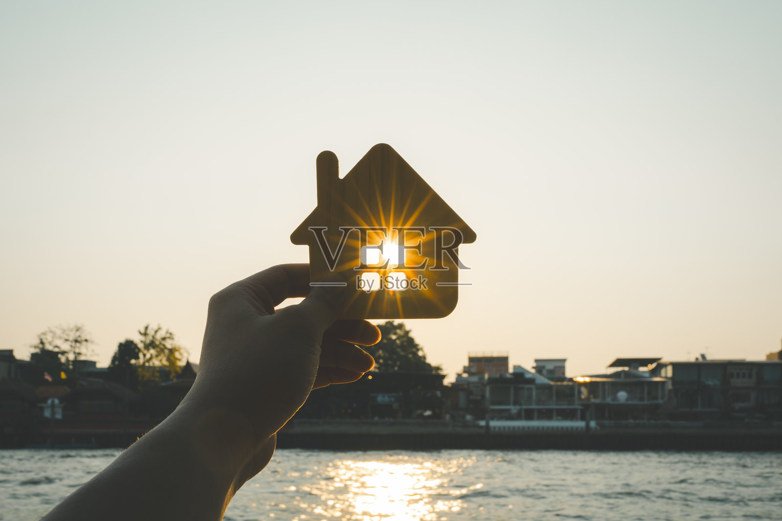 房屋保险经纪人手中的房屋模型以建筑为背景。房地产代理提供房屋、财产保险的概念。照片摄影图片