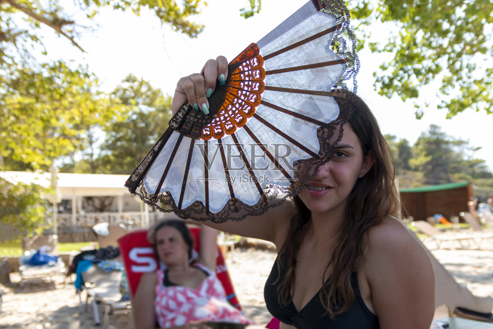 一个穿着泳装的年轻女子看着镜头，手里拿着一把扇子遮住了半边脸照片摄影图片