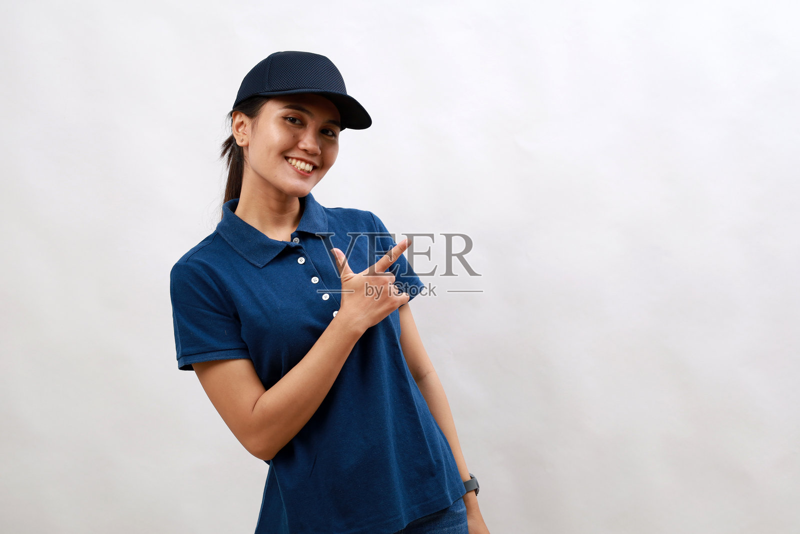 年轻的亚洲女快递员穿着快递制服，戴着帽子，笑容满面，用手和手指指着一边，脸上带着快乐和自然的表情照片摄影图片