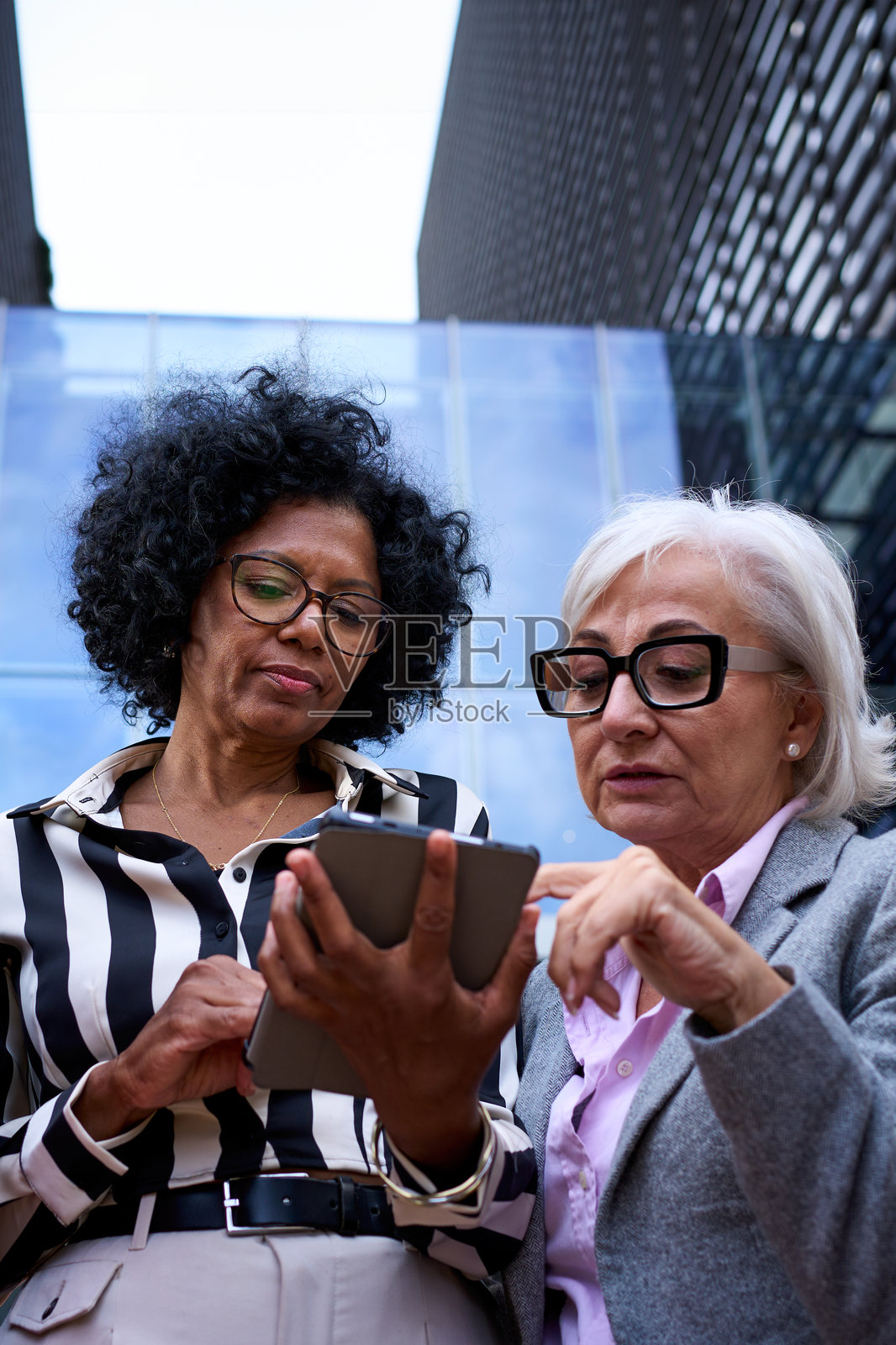 低角度。几个不同的商业女性聚集在户外，集中使用和手持平板电脑。照片摄影图片