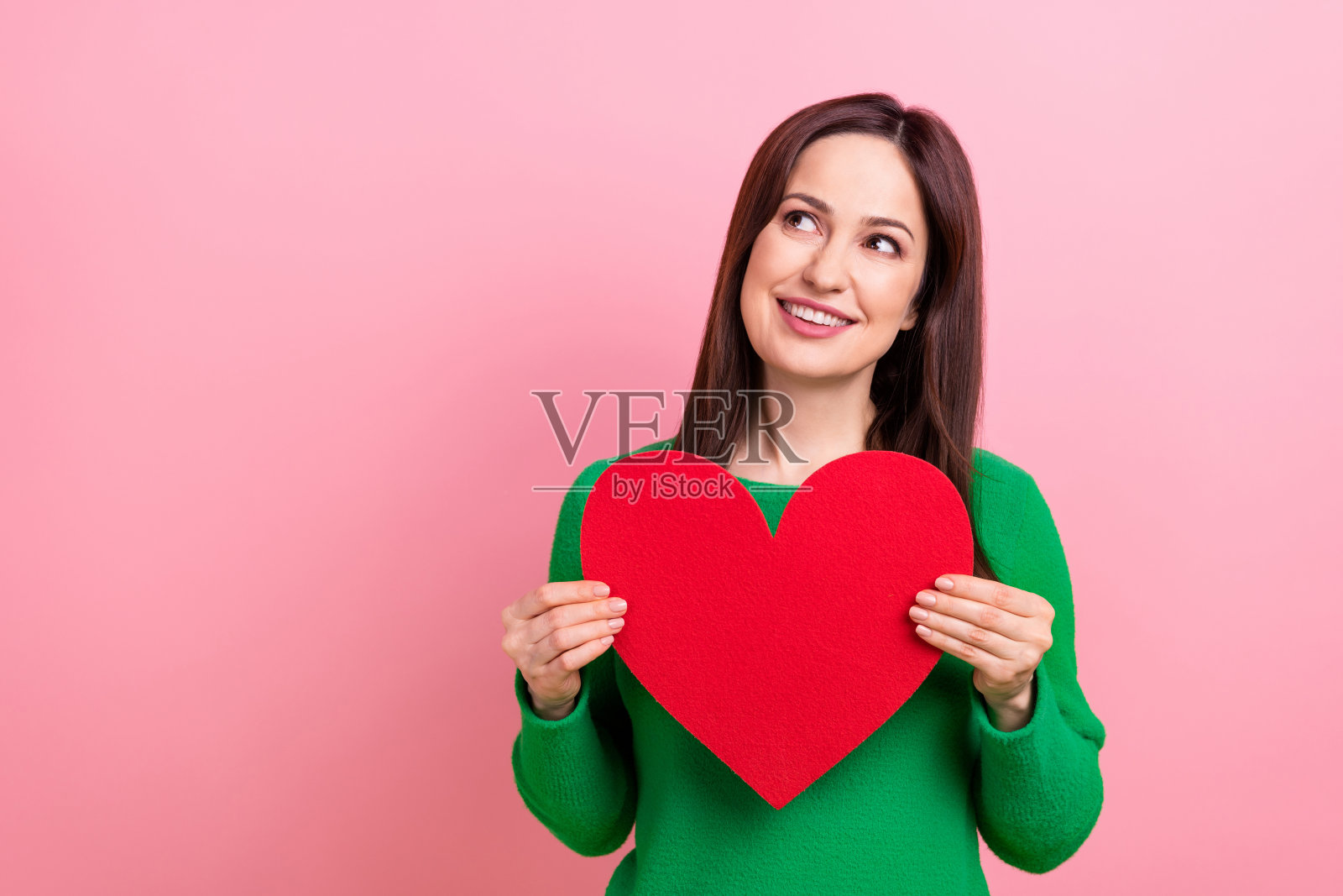 照片中开朗梦幻的女人穿着绿色的毛衣上升的心看起来空旷的空间孤立粉红色的背景照片摄影图片
